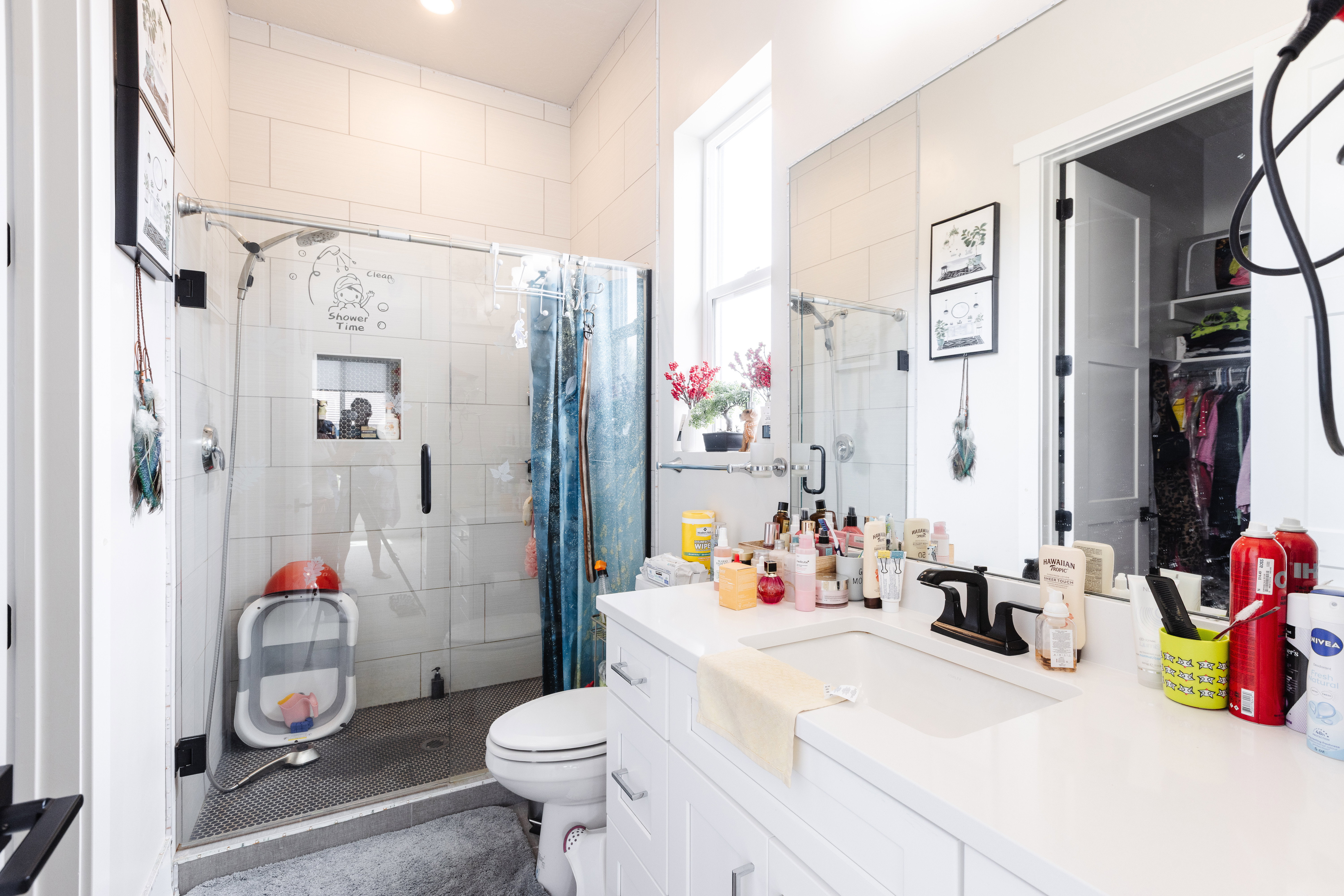 Bright bathroom featuring a glass-enclosed shower with white subway tile, a vanity with a white countertop and dark-finish faucet, a large mirror, and a window for natural light