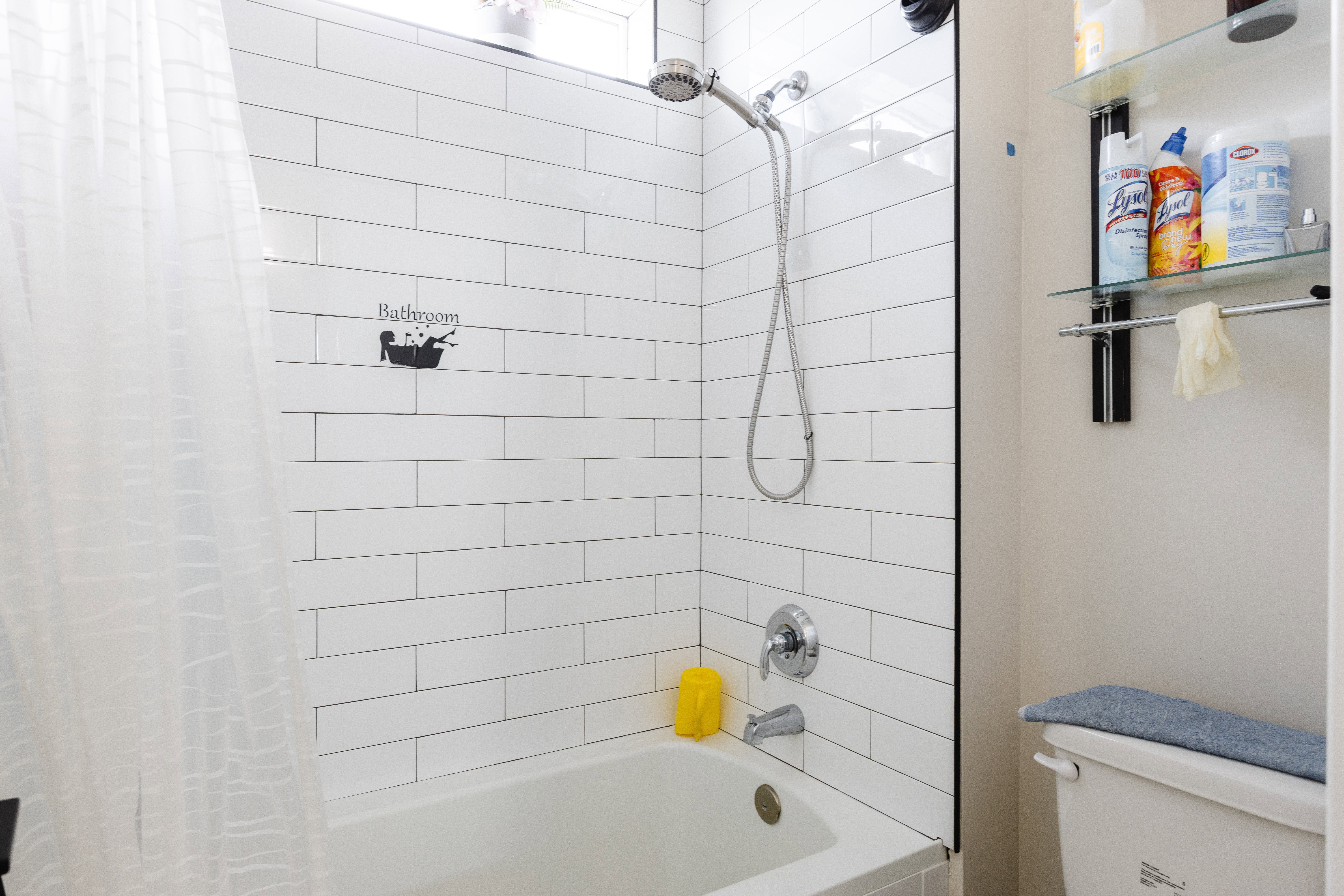 Tub and shower combination featuring white subway tile surround with dark grout, chrome fixtures, and a clear glass shower screen
