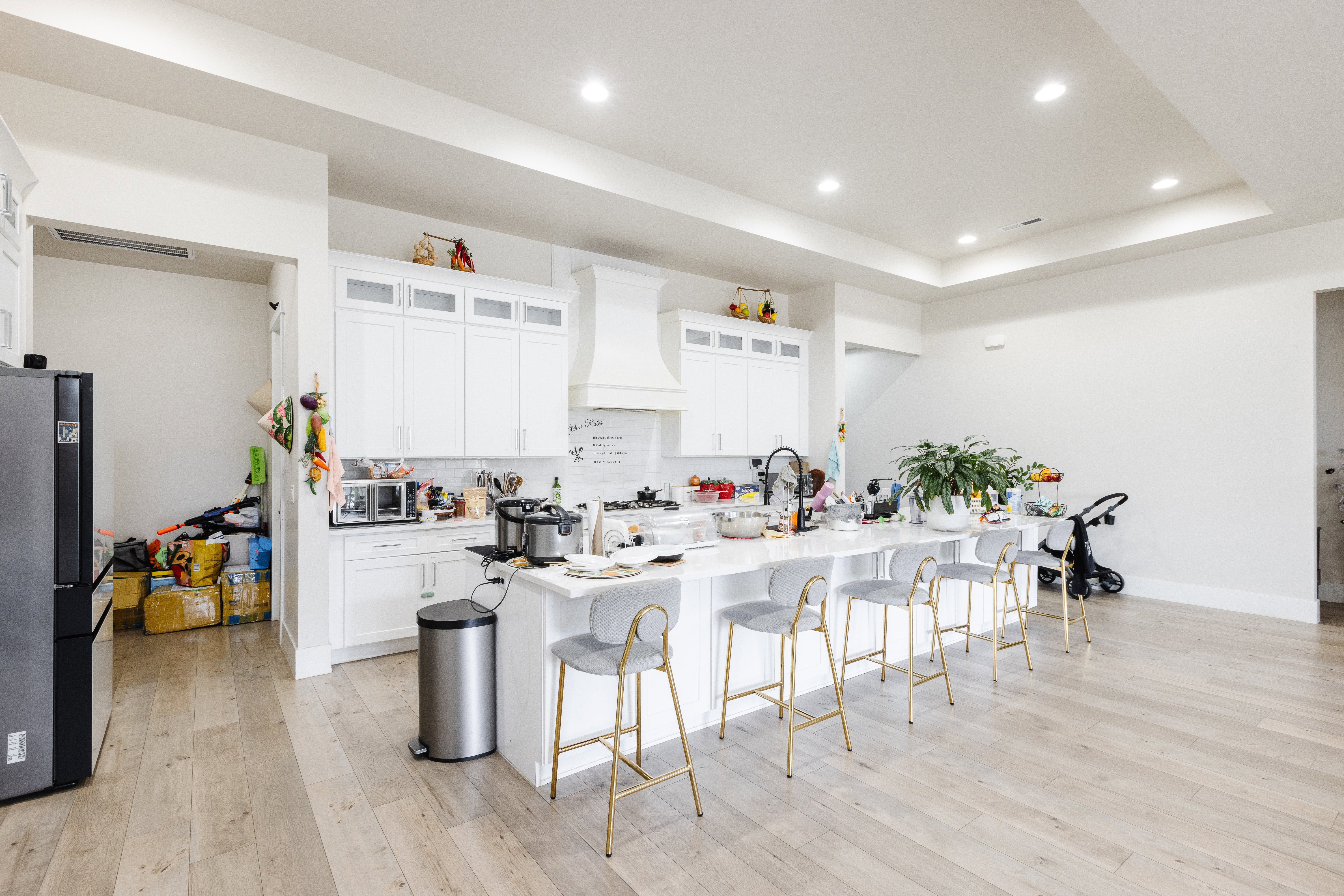 Contemporary kitchen featuring a spacious island with seating, white cabinetry, integrated range hood, recessed lighting, and wood-finish flooring