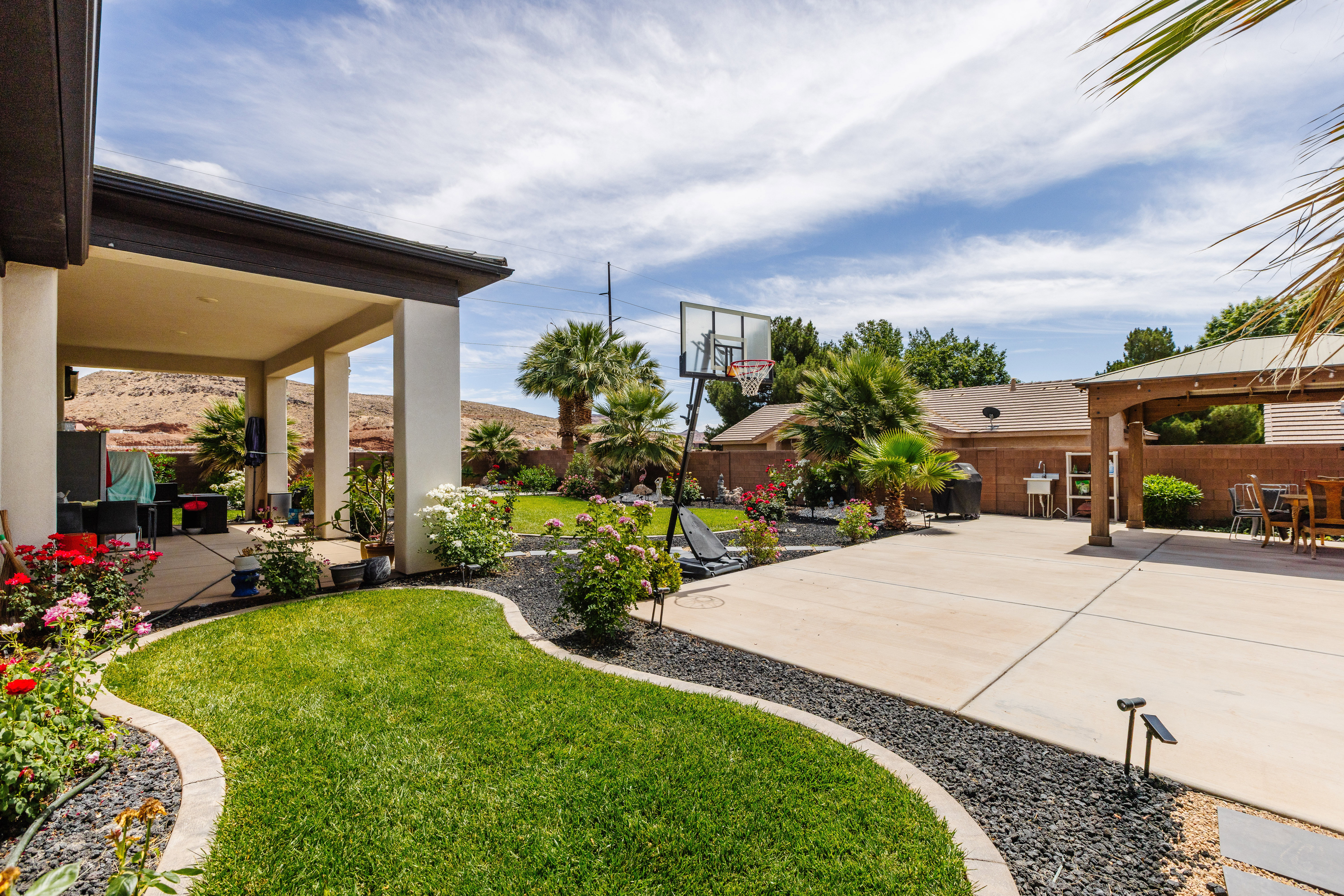 Expansive backyard featuring a covered patio, concrete paving, and a manicured lawn