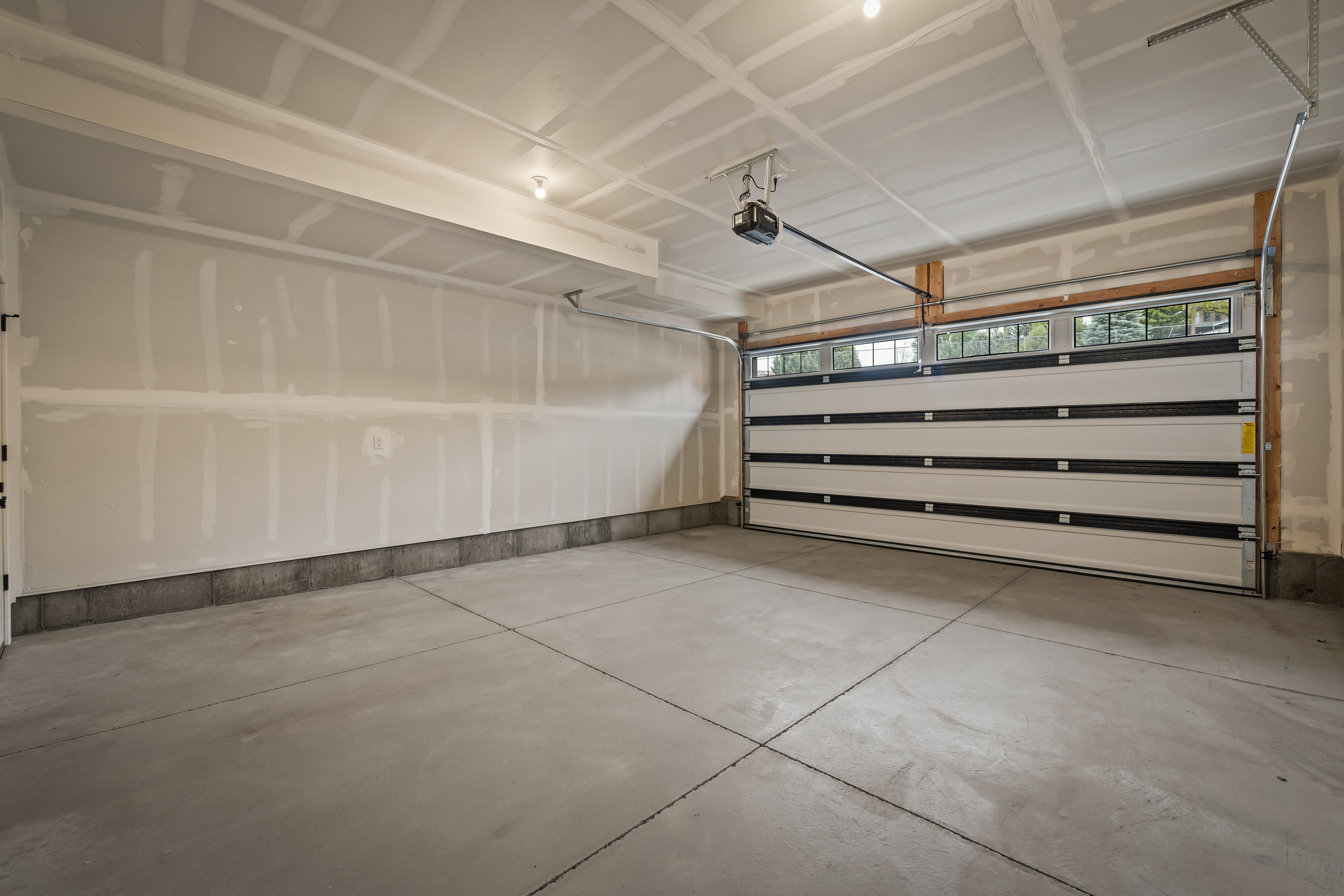 Two-car garage featuring a segmented overhead door with upper window panels, concrete flooring, and an automatic garage door opener