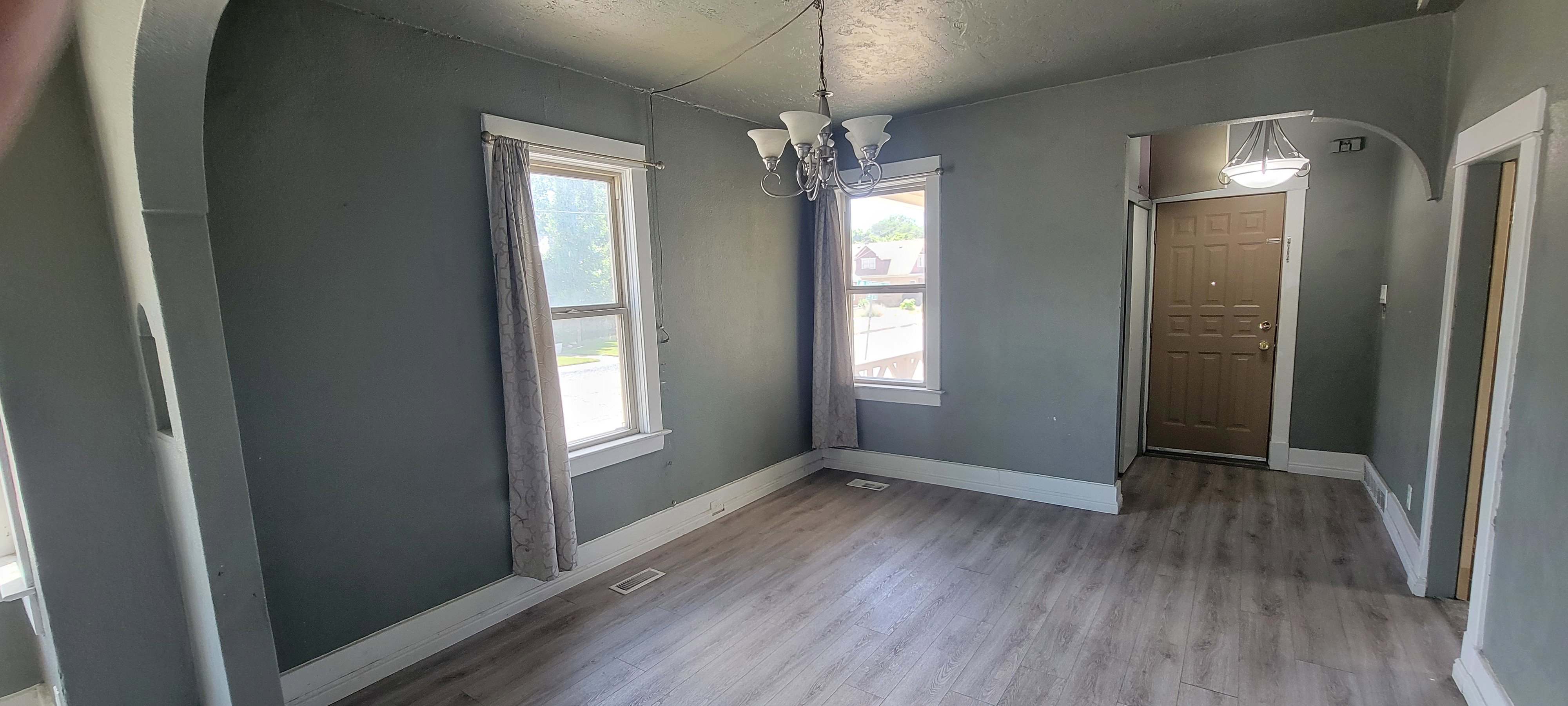 Open concept living space featuring wood-finish flooring, multiple windows, a decorative chandelier, and an arched entryway