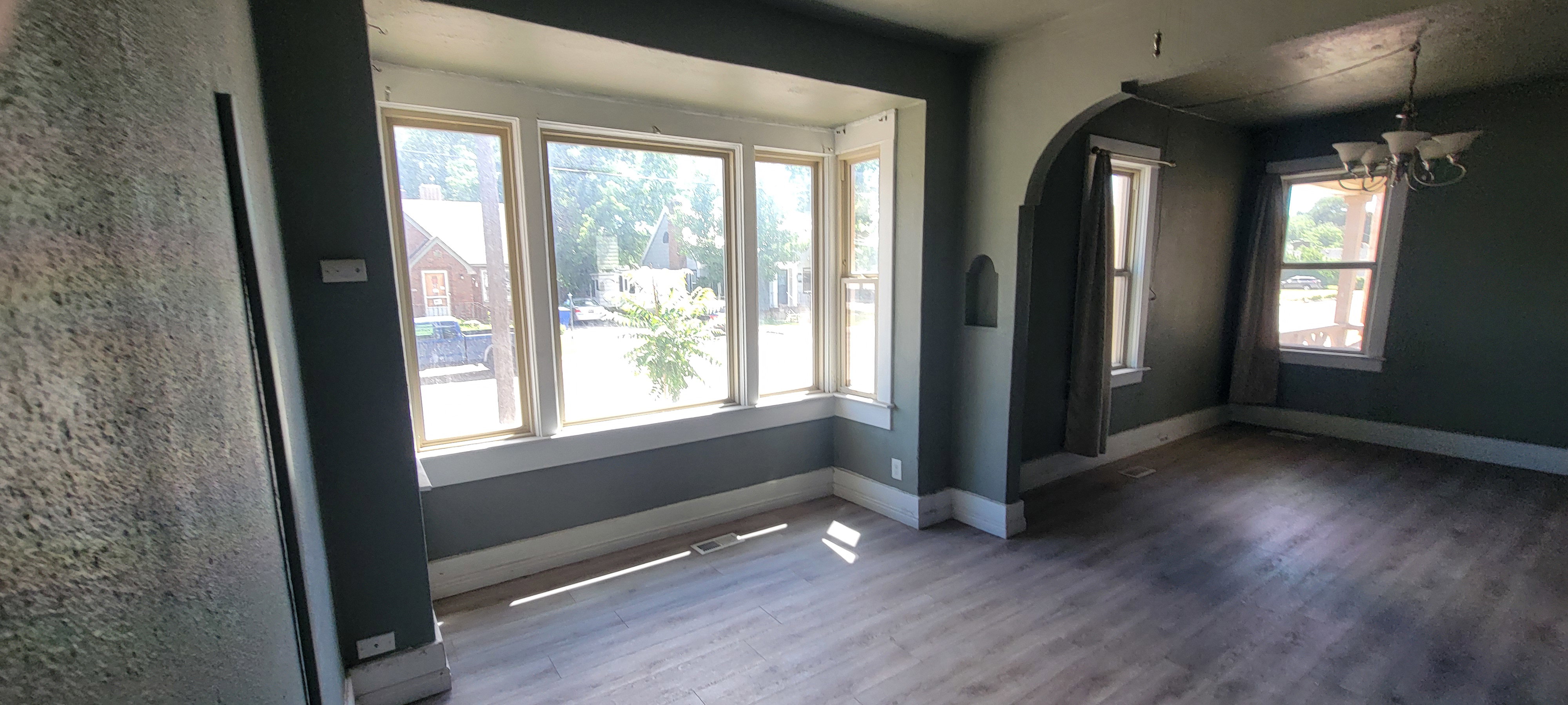 Bay window with white trim, wood-finish flooring, recessed wall niche, and an arched doorway