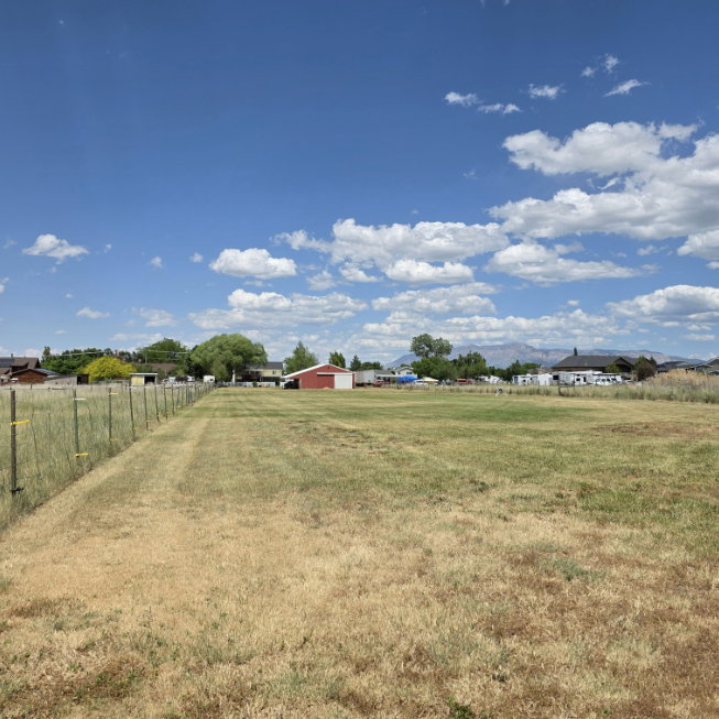 Expansive open field featuring a partial perimeter fence and distant mountain range