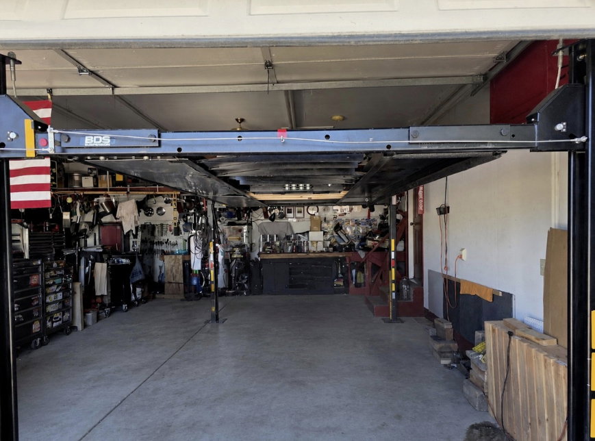 Spacious garage featuring a four-post car lift, concrete flooring, and ample wall storage