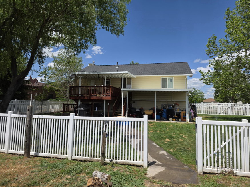 Rear elevation featuring a double-level deck, covered patio, white picket fencing, and mature trees