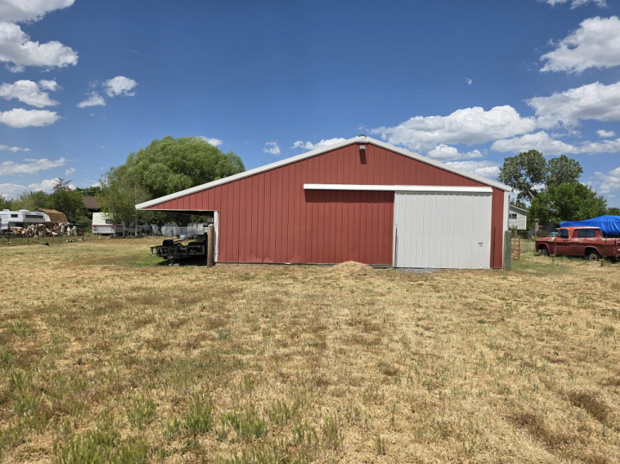 Red metal barn structure featuring a white sliding door, an extended overhang, and a light-colored roofline
