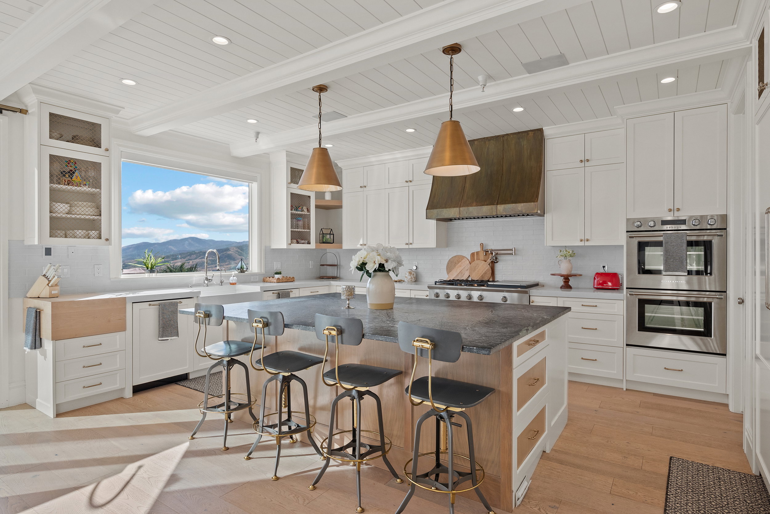Spacious kitchen featuring an expansive window, shiplap ceiling, white cabinetry, integrated double ovens, and a large central island with a dark countertop