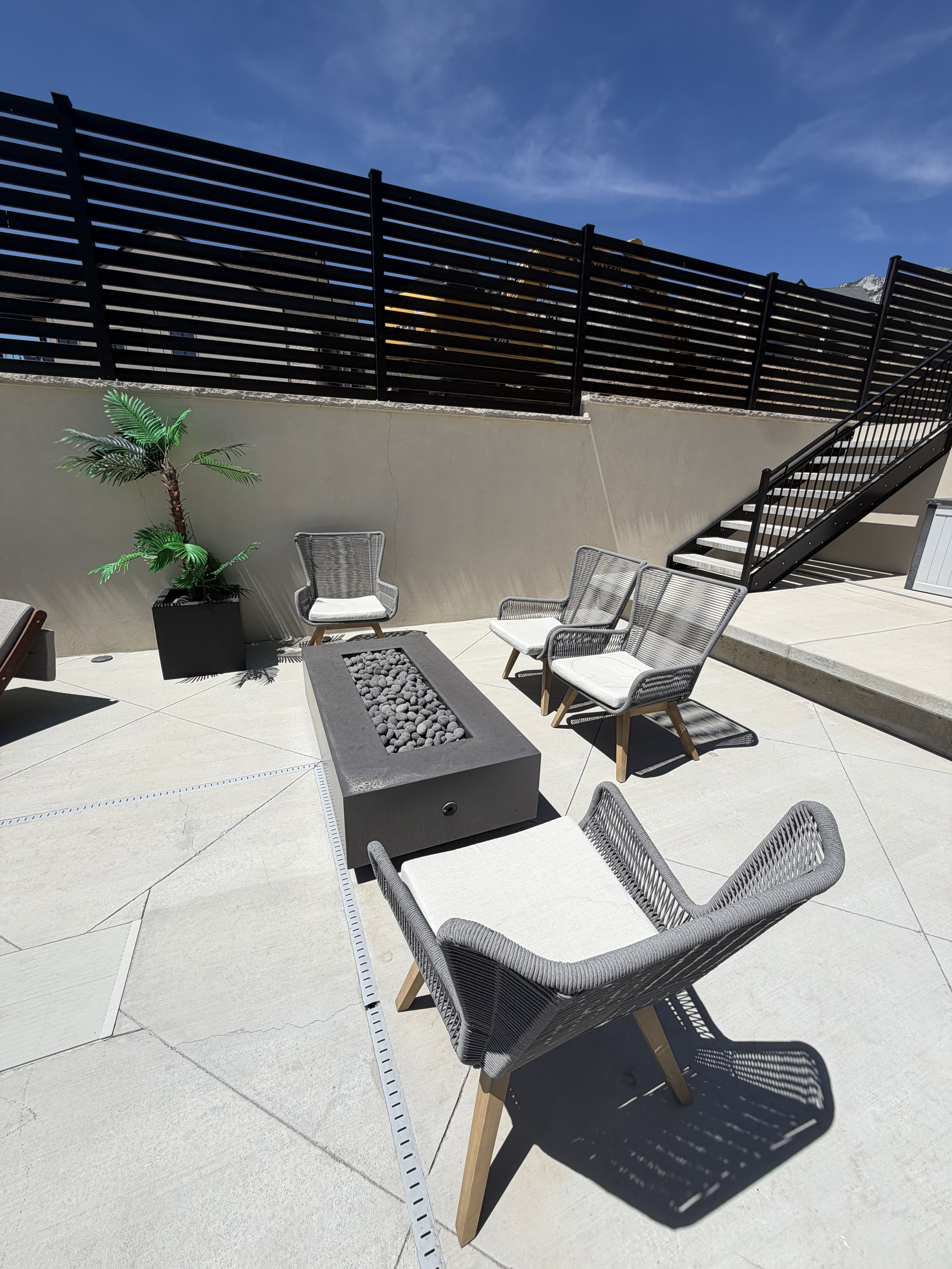 Outdoor patio featuring a rectangular fire pit with decorative stones, surrounded by light-toned pavers
