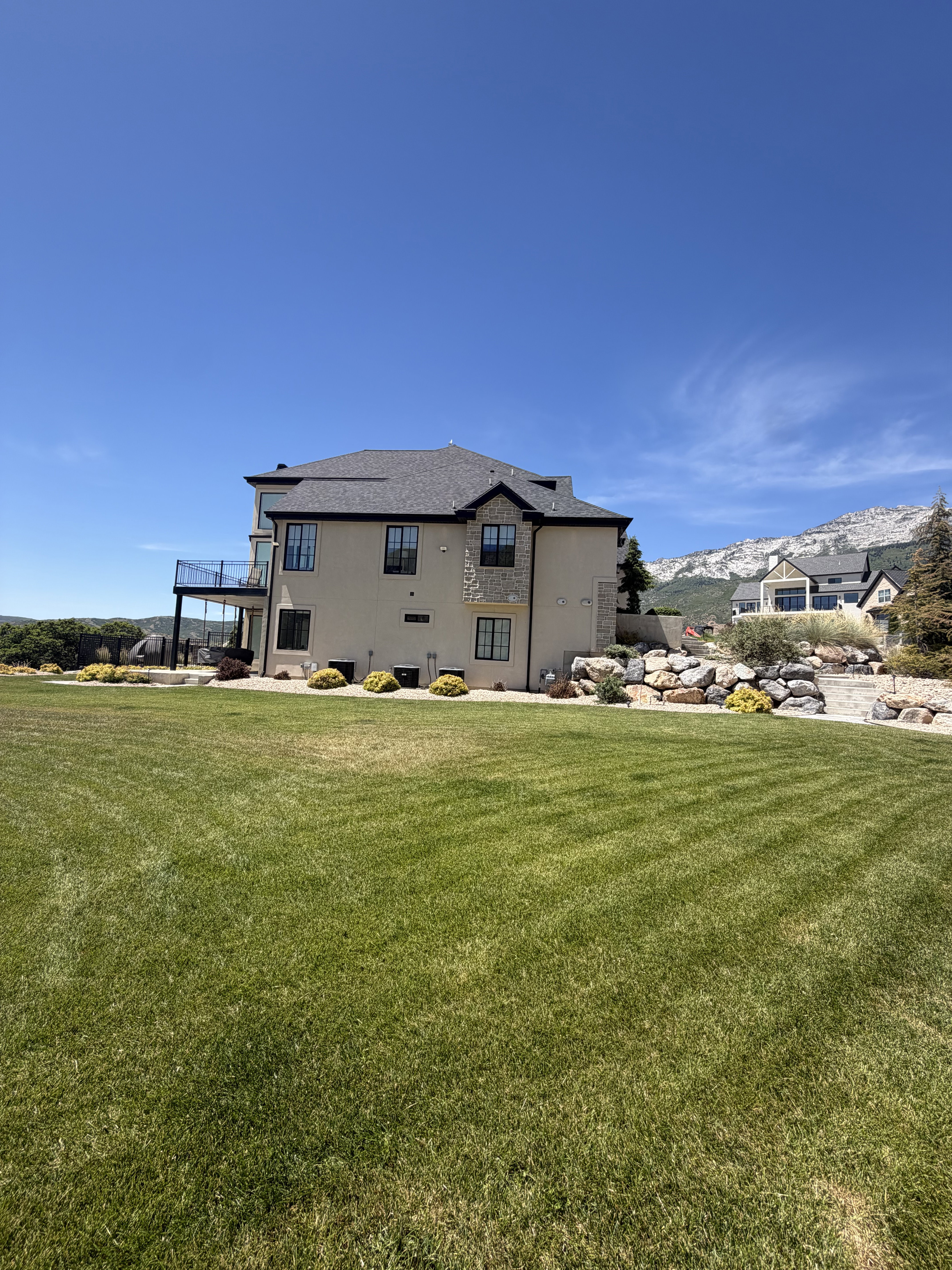 Expansive green lawn with a contemporary multi-story residence featuring a stucco and stone exterior