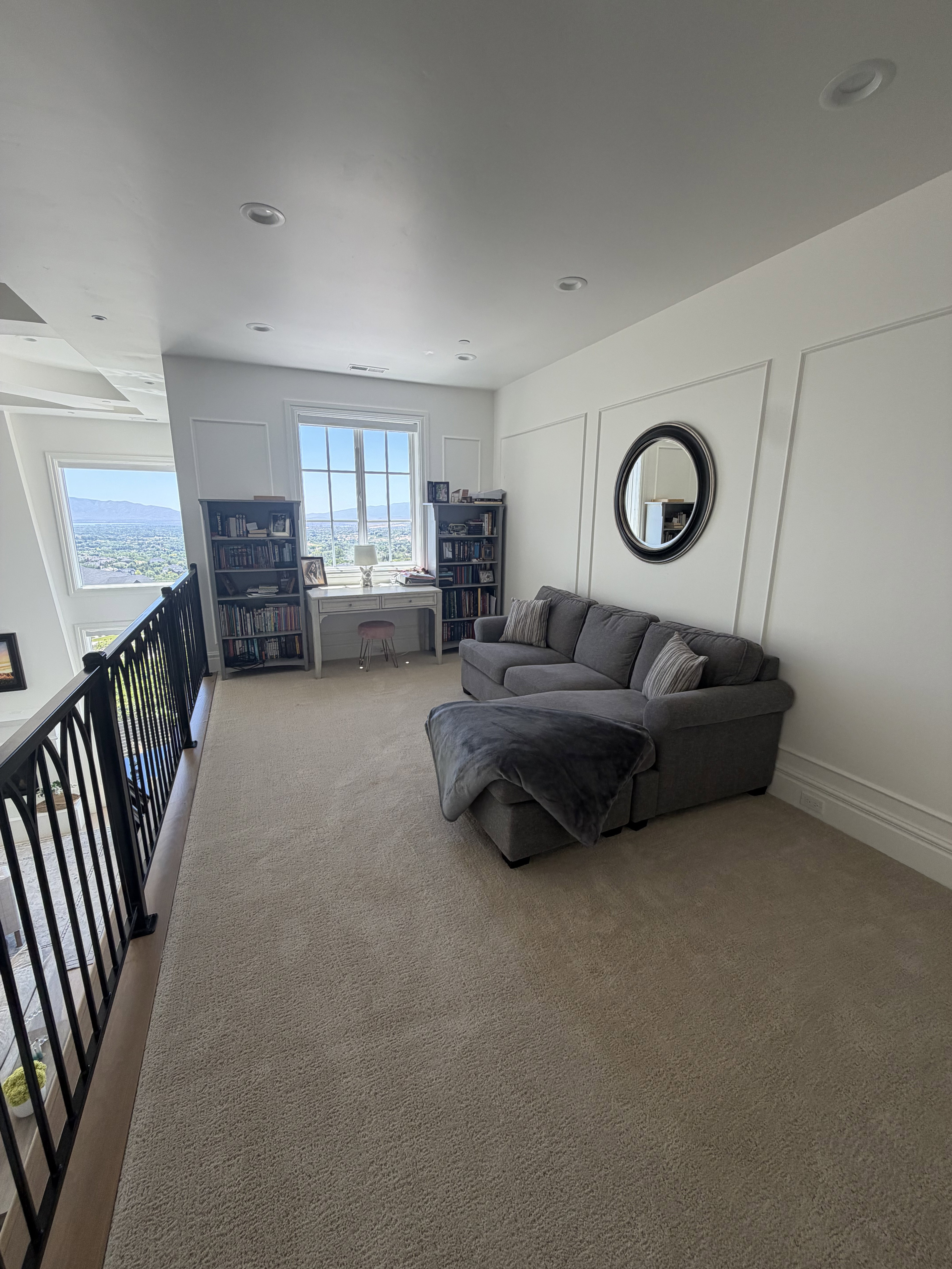Open loft area featuring neutral-toned carpeting, ample natural light from multiple windows, recessed lighting, decorative wall paneling, and a black wrought iron railing