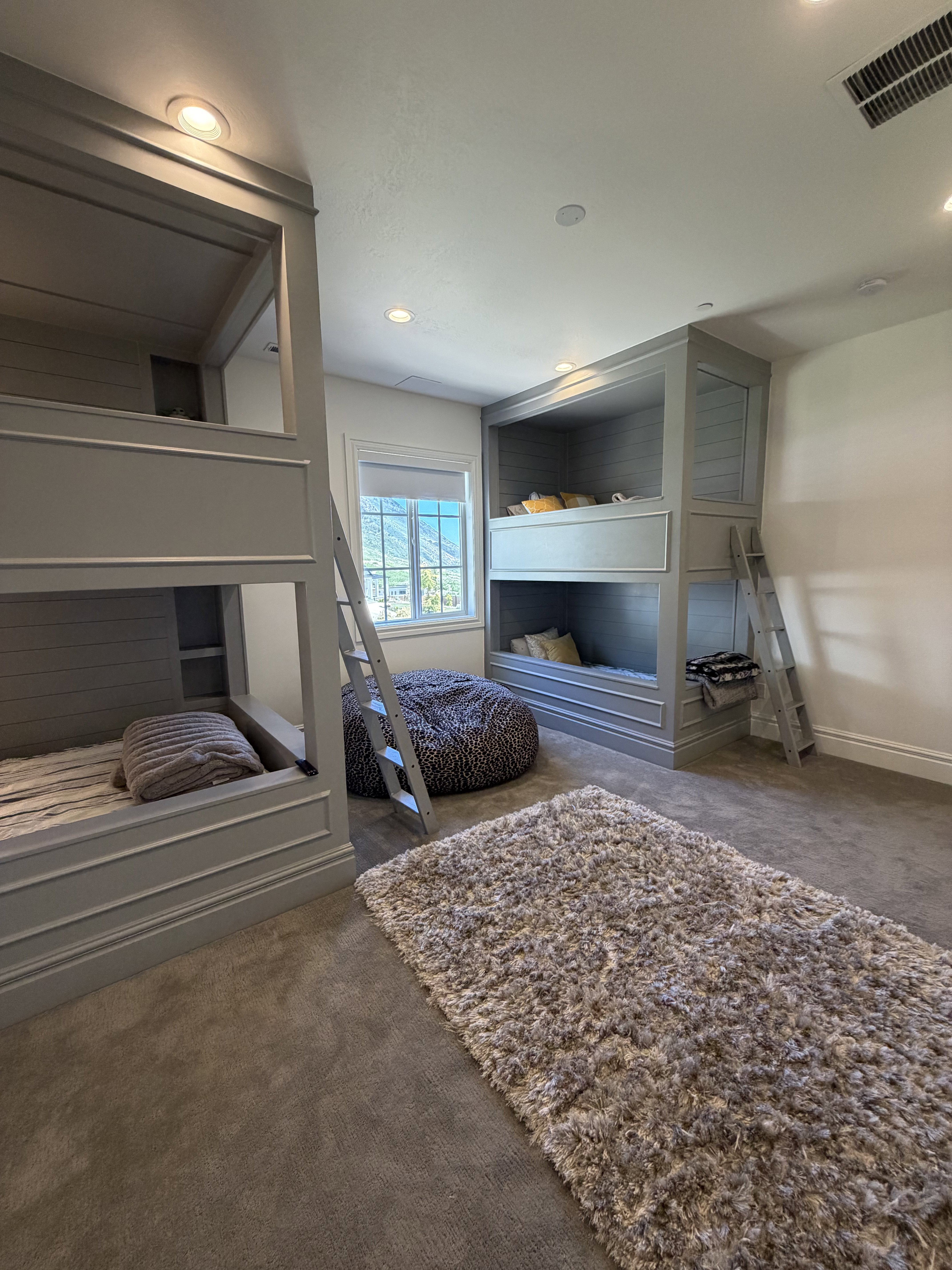 Room featuring two built-in bunk bed structures with integrated ladders and storage, recessed ceiling lighting, and a window providing natural light