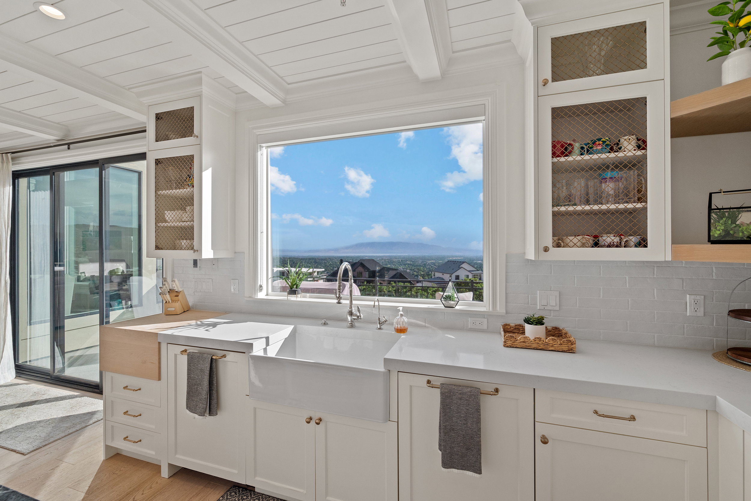 Kitchen featuring white cabinetry, a large farmhouse sink, stone countertops, a subway tile backsplash, and a large window overlooking a distant landscape