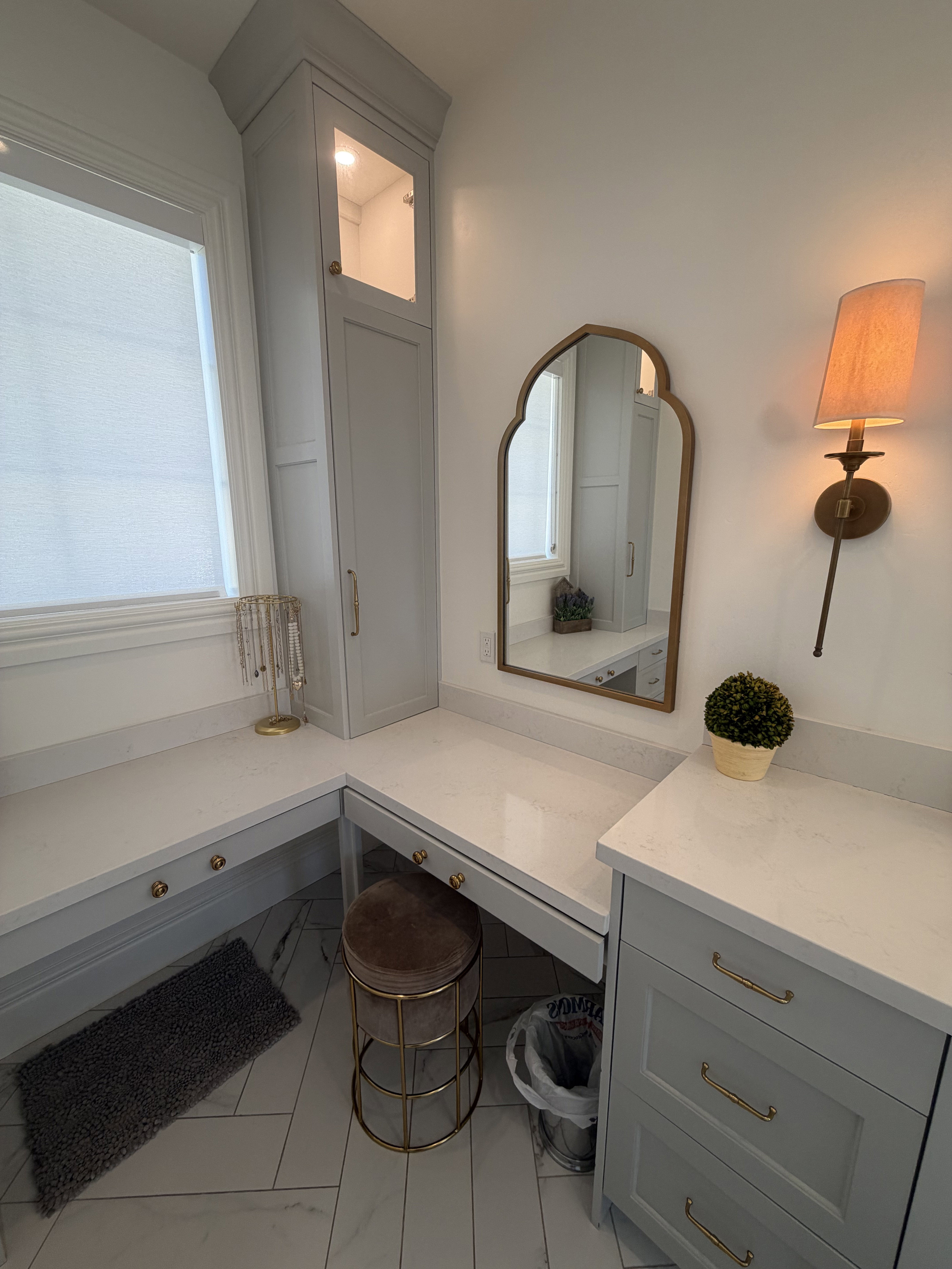 Built-in vanity with quartz countertops, custom gray cabinetry, and brass hardware