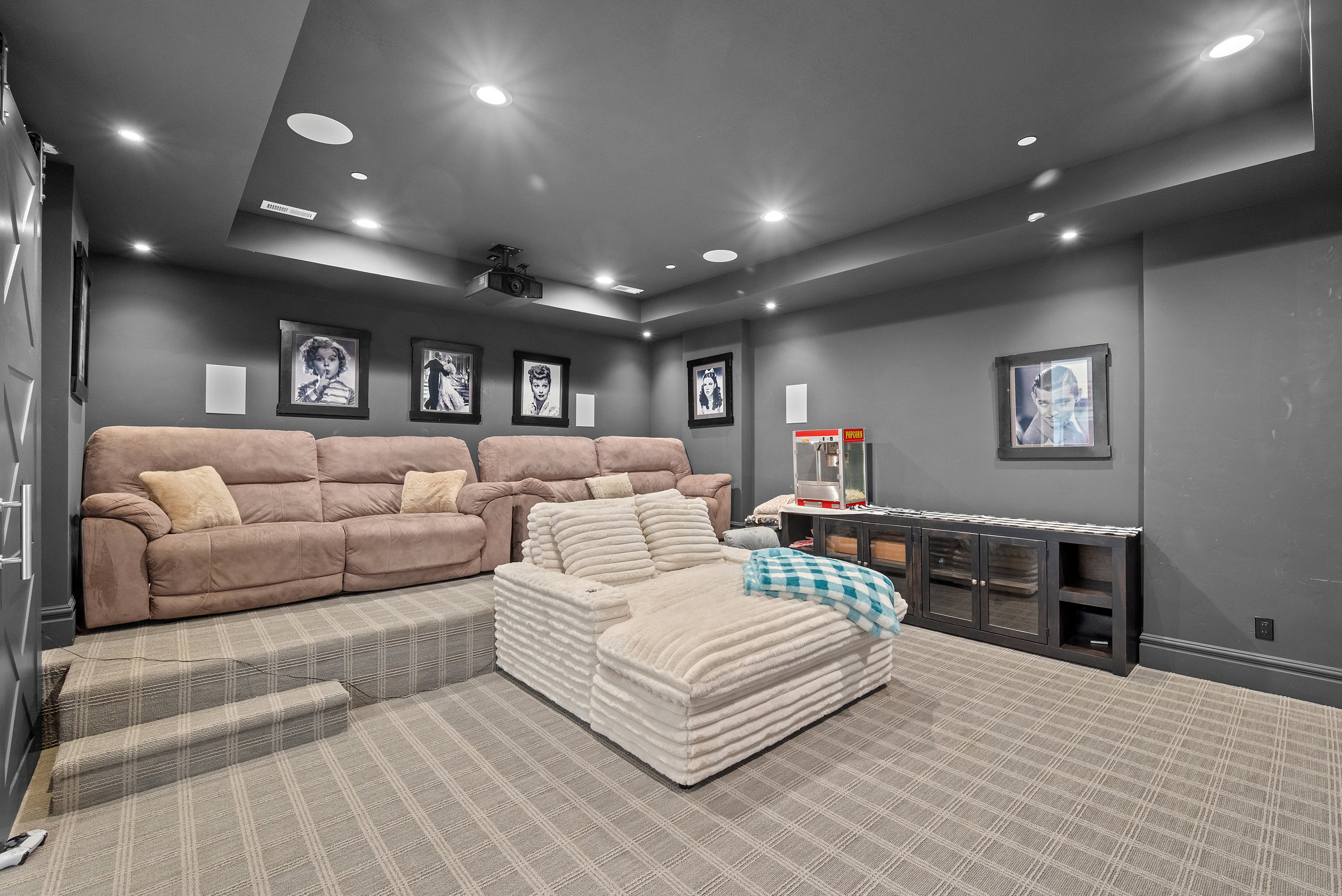 Dedicated media room featuring tiered seating, recessed lighting, a ceiling-mounted projector, and integrated ceiling speakers