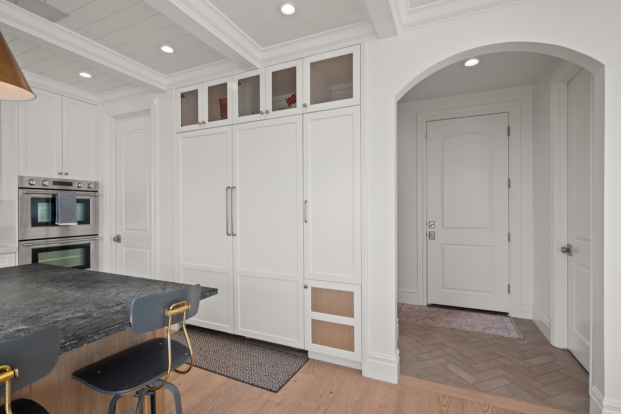 Kitchen featuring integrated panel-front appliances, double wall ovens, a coffered ceiling with recessed lighting, and an arched entryway