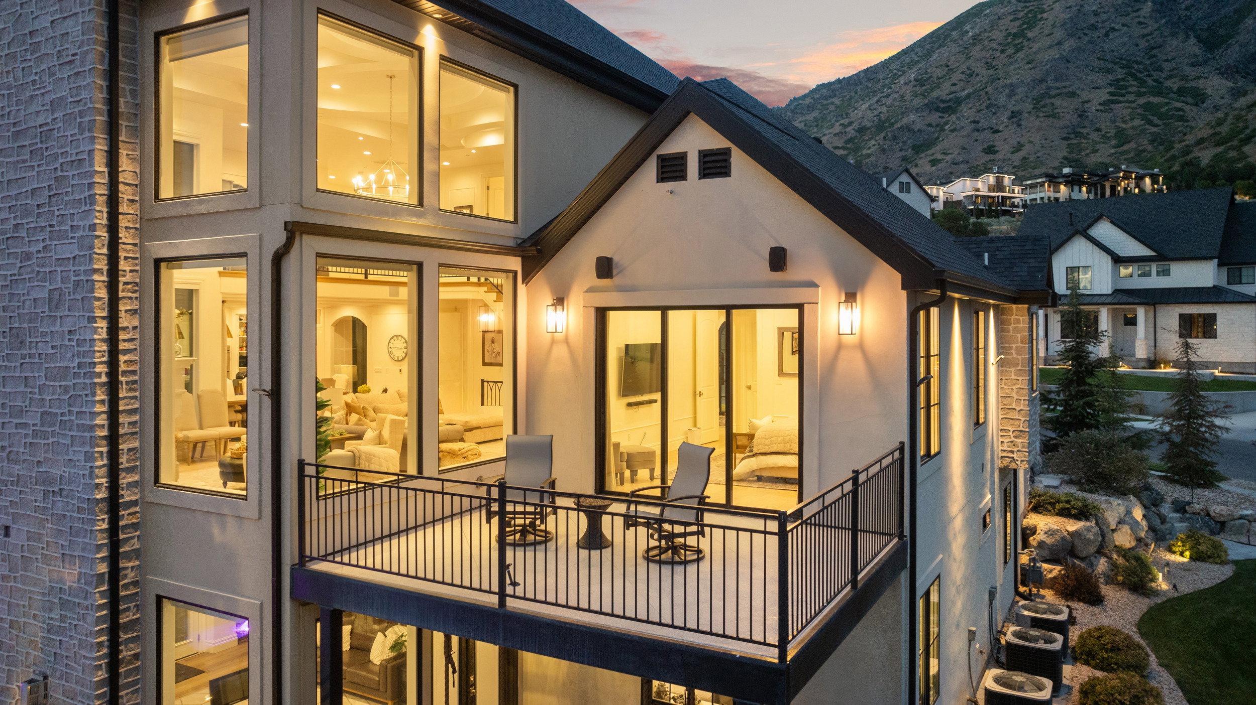 Exterior featuring a private balcony with black metal railing, multiple large windows, stucco and stone facade, and a pitched roofline