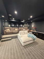 Dedicated media room featuring tiered seating, recessed lighting, ceiling-mounted projector, built-in speakers, and patterned carpet flooring