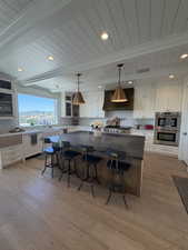 Spacious kitchen featuring white shaker cabinetry, an expansive center island with dark countertops, built-in stainless steel double ovens, and wood-finish flooring