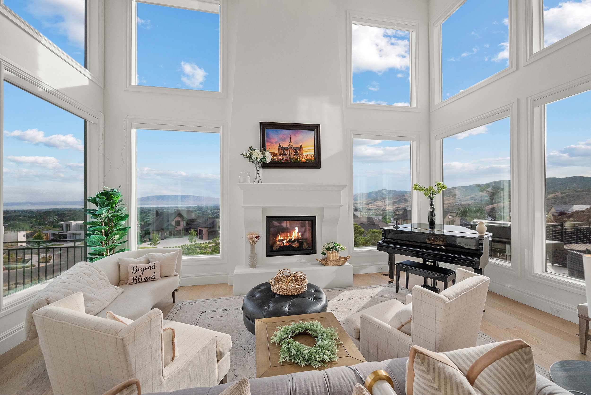 Two-story living area featuring a fireplace with a white mantel, large windows, light wood-finish flooring, and white walls