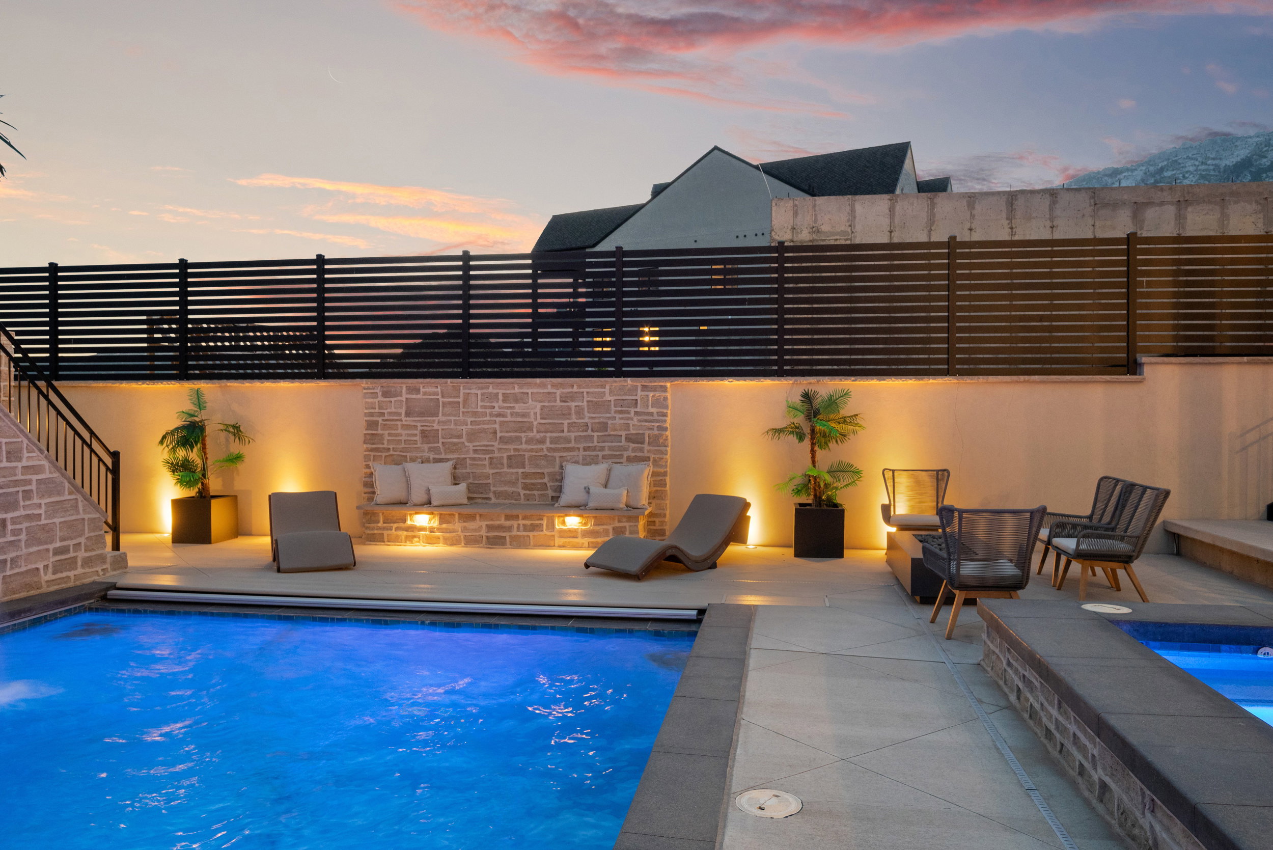 Illuminated outdoor living space featuring a swimming pool, stone accent wall with built-in seating, and integrated wall lighting