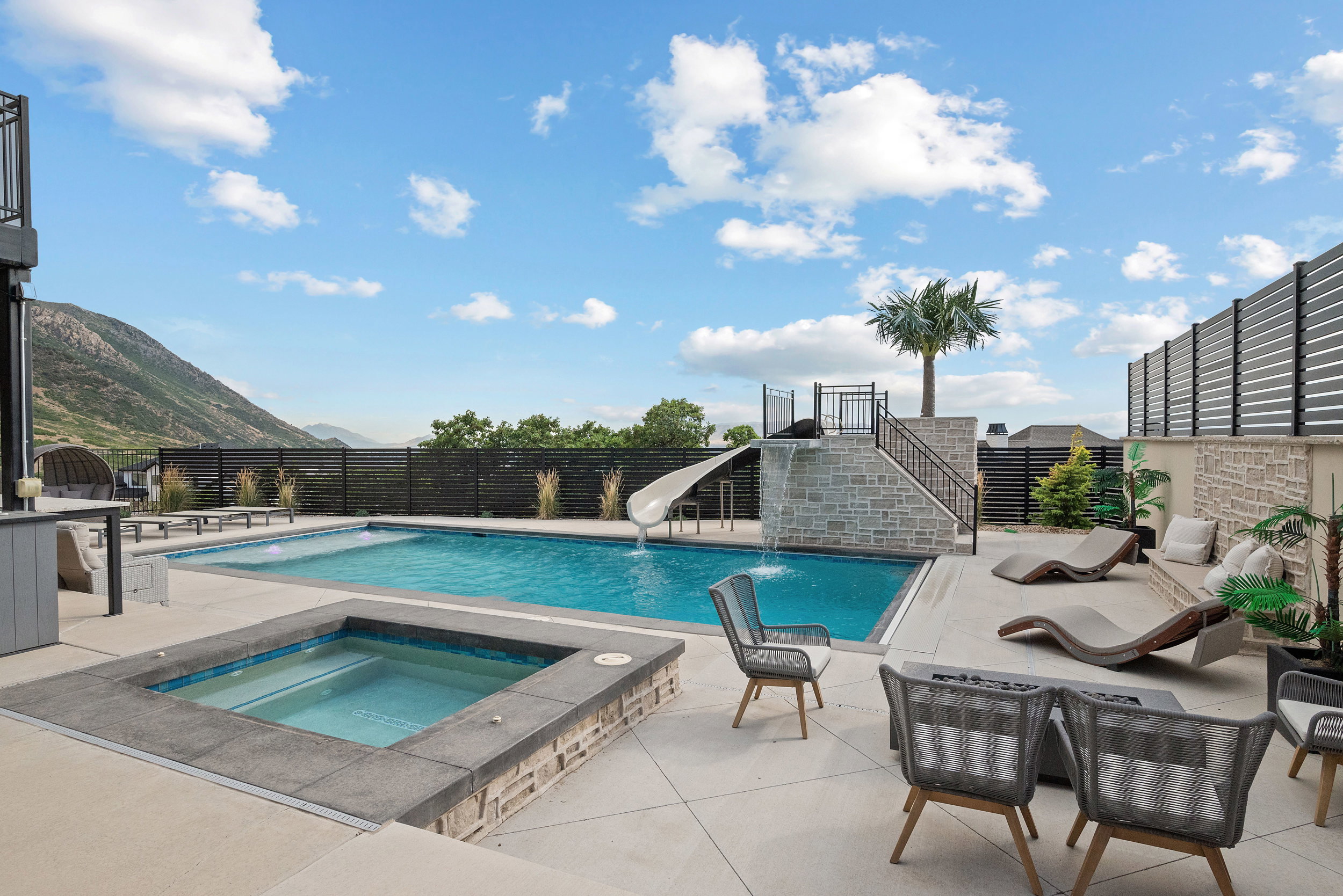 Expansive outdoor living area featuring a rectangular swimming pool, integrated spa, and a stone-clad water slide structure