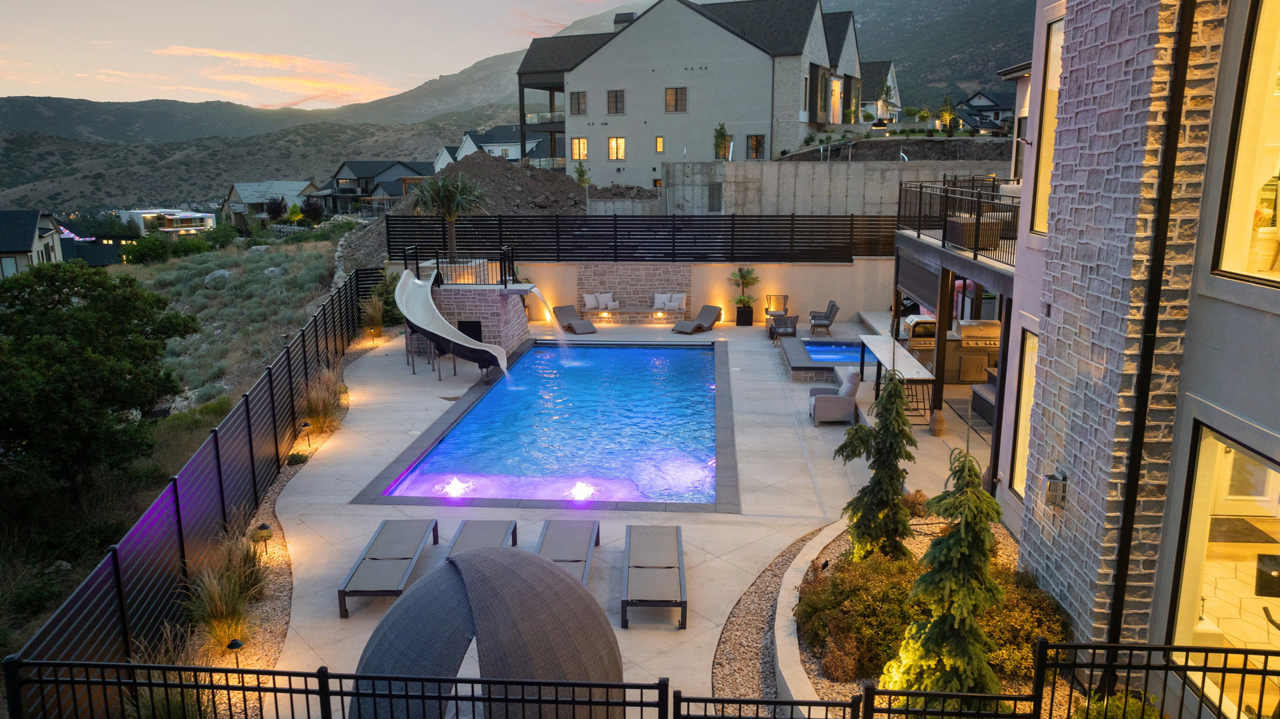 Expansive outdoor entertainment area featuring a large swimming pool with integrated slide, an adjacent spa, and a built-in outdoor kitchen with bar seating