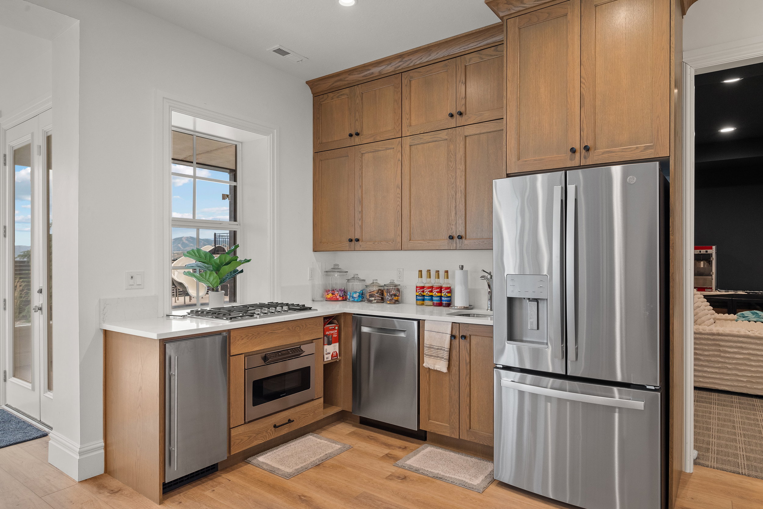 Kitchenette featuring wood-finish flooring, light wood cabinetry, white countertops, and stainless steel appliances including a refrigerator, dishwasher, and microwave