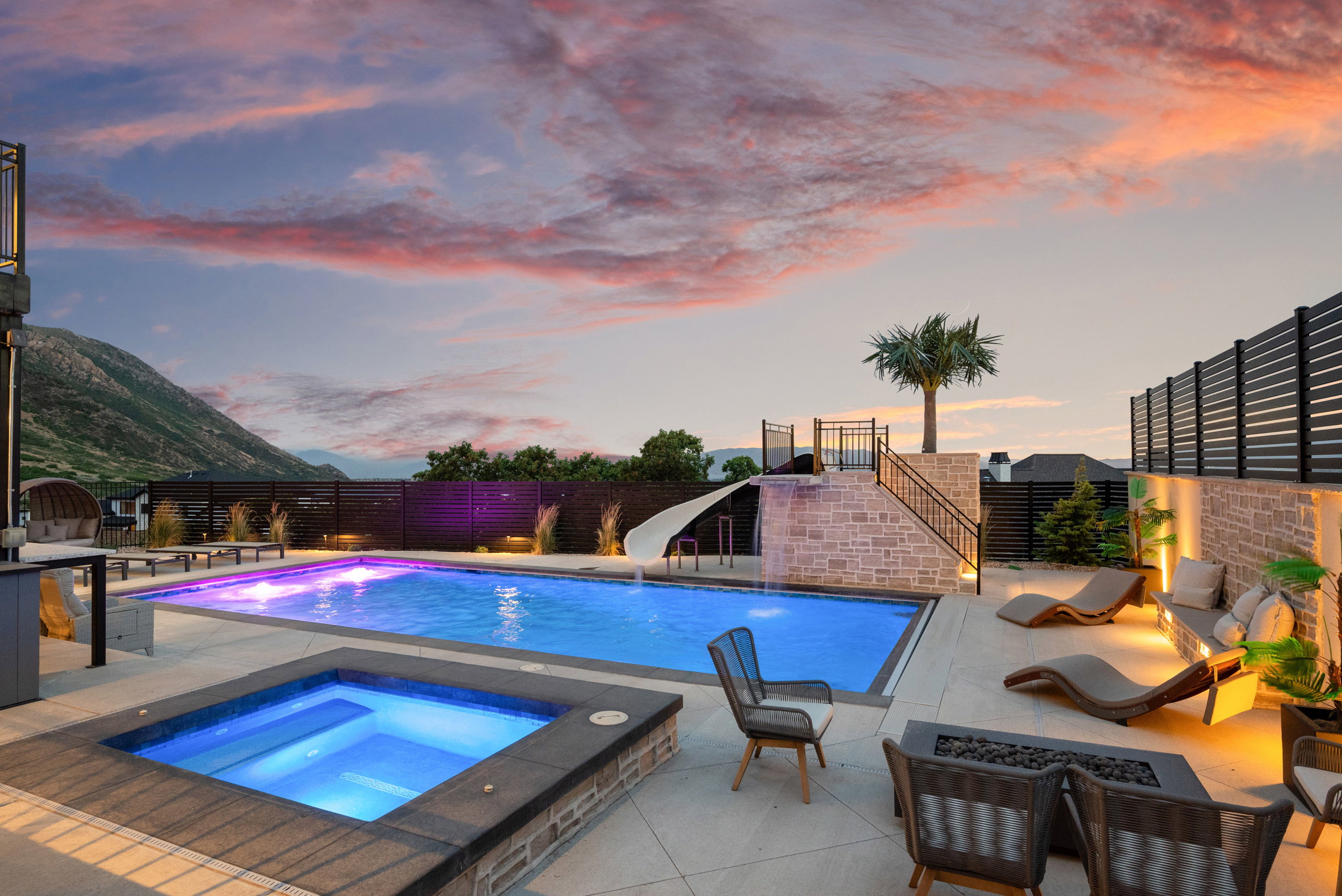 Resort-style backyard featuring a rectangular swimming pool with integrated lighting, a separate square spa, and a stone-clad water slide structure