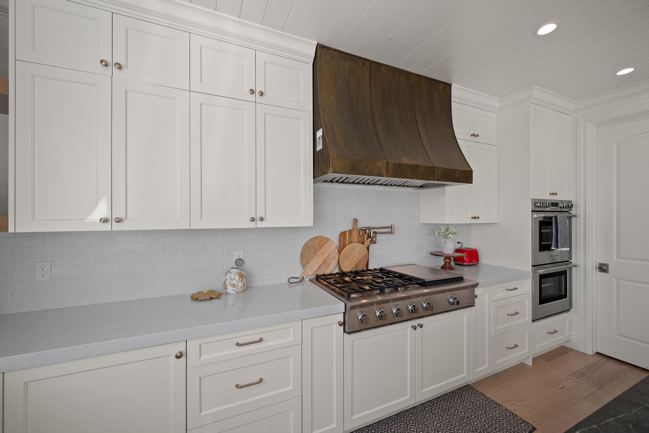 Kitchen featuring white shaker cabinetry, stainless steel gas range with griddle, custom dark metal range hood, light-toned countertops, and subway tile backsplash