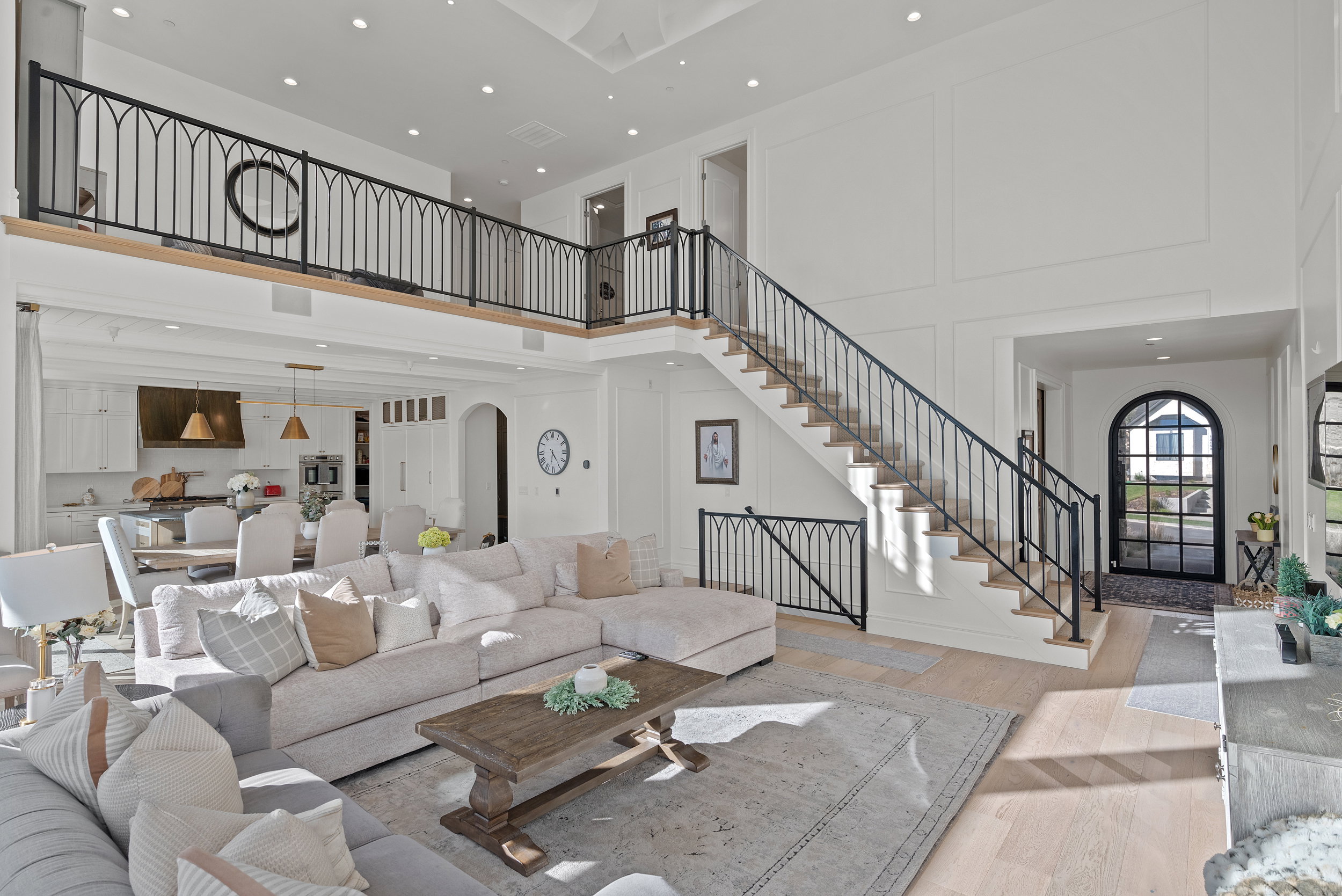 Two-story living area featuring a grand staircase with custom wrought iron railings, an open concept kitchen with a large island, wood-finish flooring, and high ceilings with recessed lighting