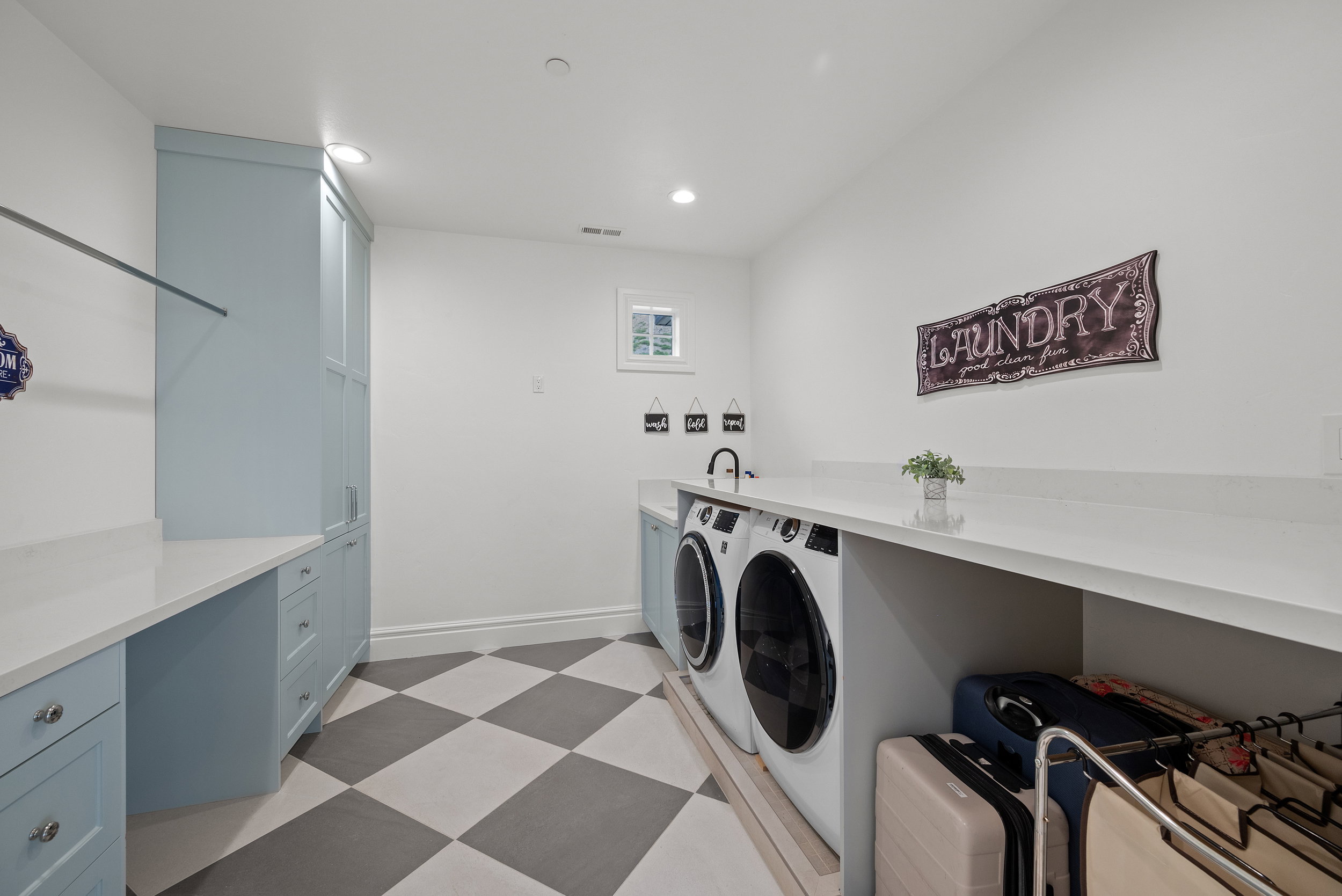 Laundry room featuring checkerboard flooring, light blue cabinetry, built-in countertops, a sink with a wall-mounted faucet, and a window
