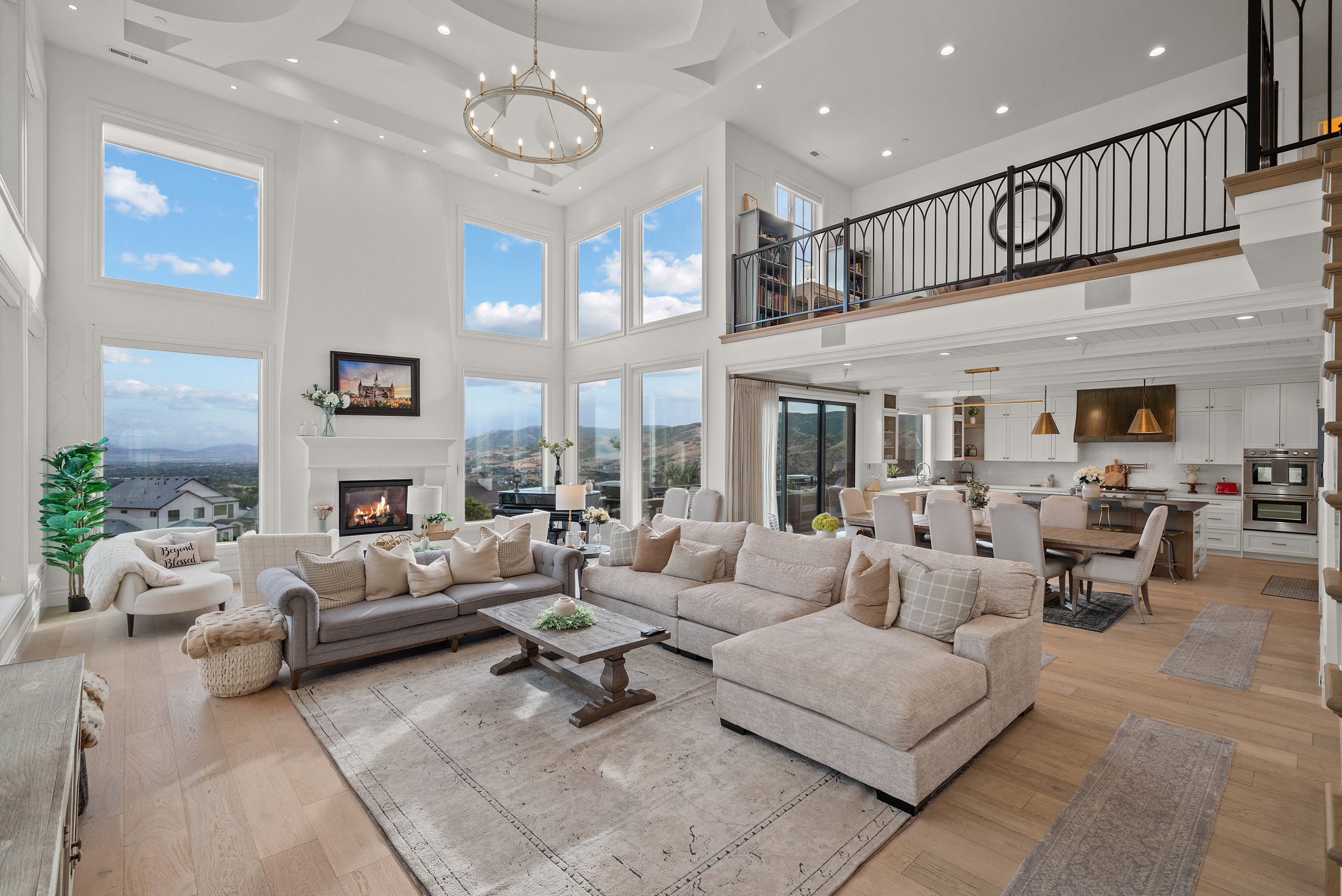 Grand living space featuring a two-story ceiling, a tiered chandelier, abundant natural light from expansive windows, and a built-in fireplace