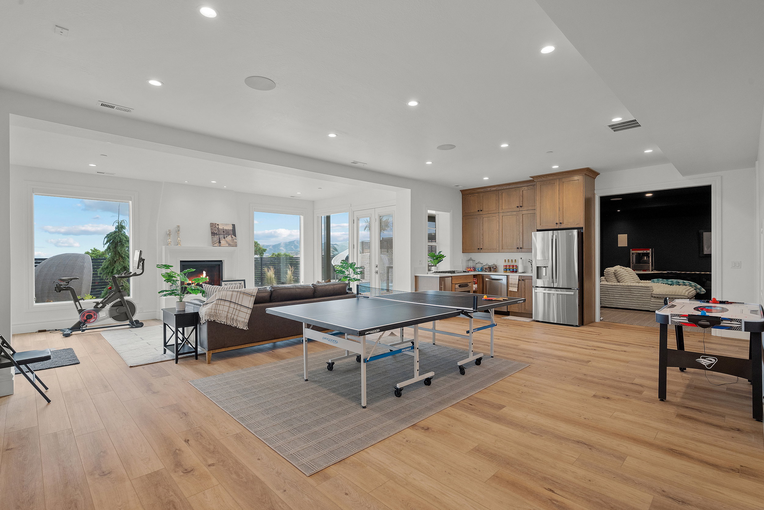 Spacious open-concept room featuring wide plank wood-finish flooring, recessed lighting, and a built-in wet bar with wood cabinetry and stainless steel appliances