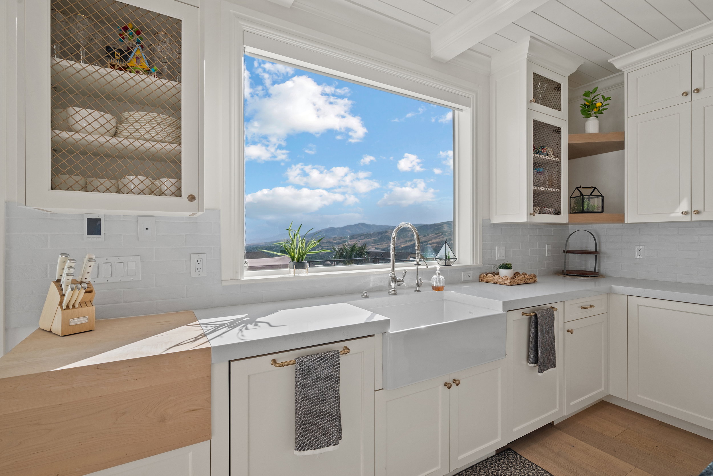 Kitchen featuring a farmhouse sink with chrome faucet, light wood-finish flooring, white shaker cabinetry, and light-toned countertops