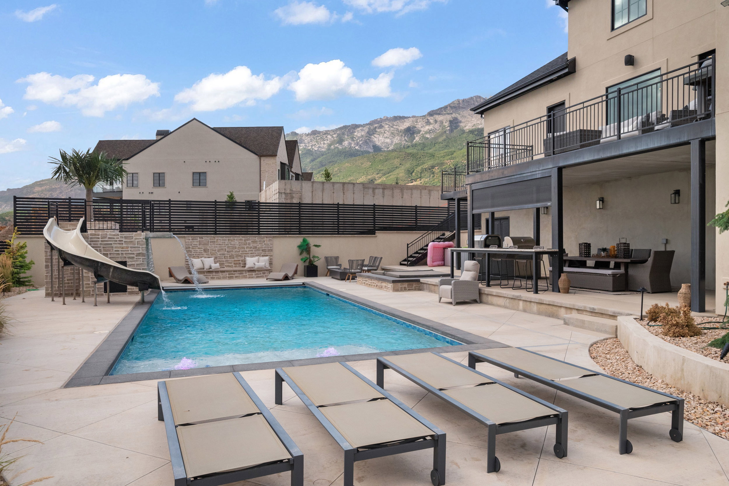 Expansive concrete patio area featuring a rectangular swimming pool with integrated slide and water features
