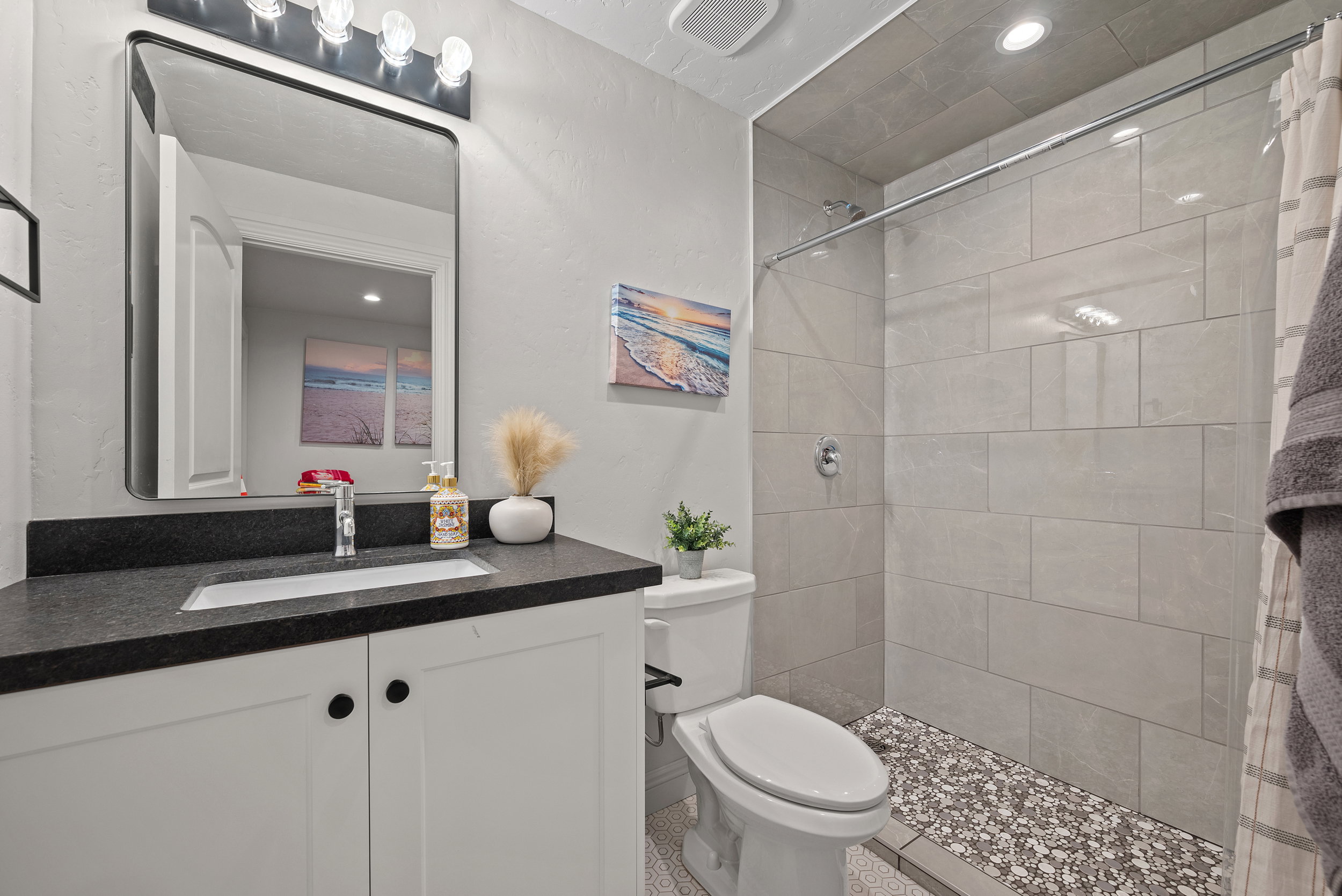 Bathroom featuring a white vanity with black countertop, rectangular undermount sink, and a framed mirror