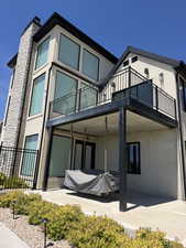 Modern stucco exterior featuring a stone-clad chimney and a balcony with black metal railings