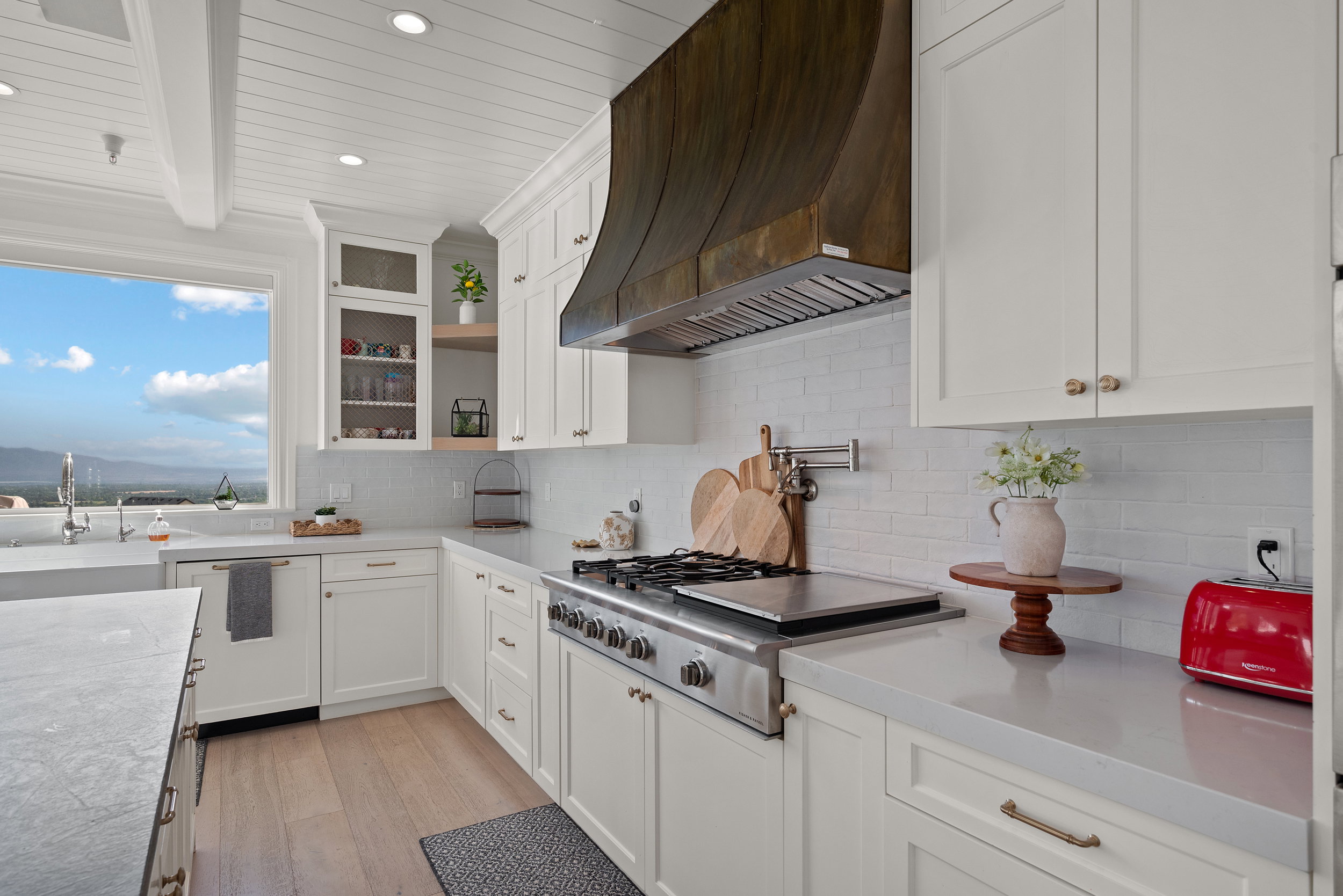 Kitchen with a large window, white shaker cabinetry, stainless steel range, and a wood-finish range hood