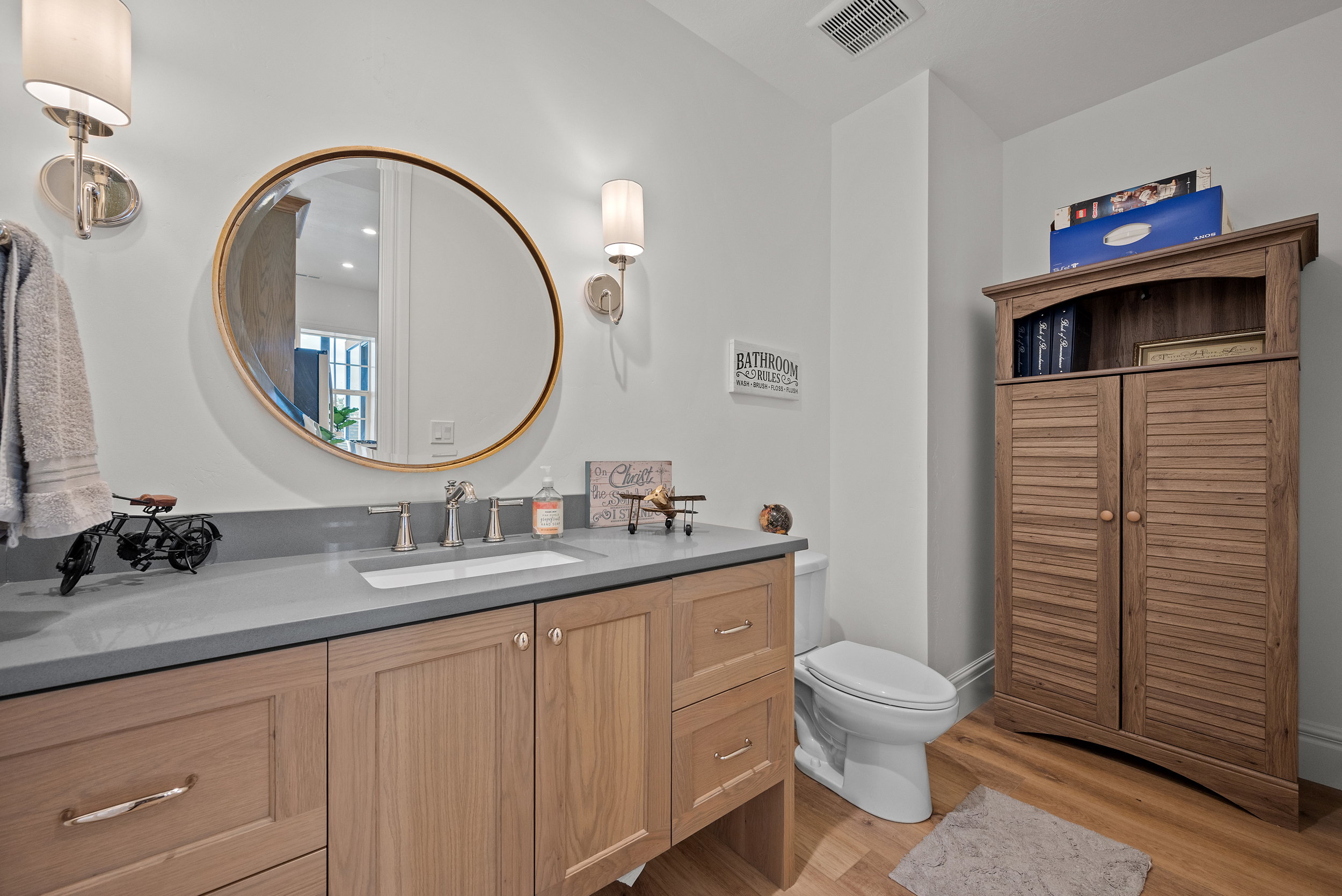 Bathroom featuring a light wood-finish vanity with a built-in sink and gray countertop, complemented by a round framed mirror
