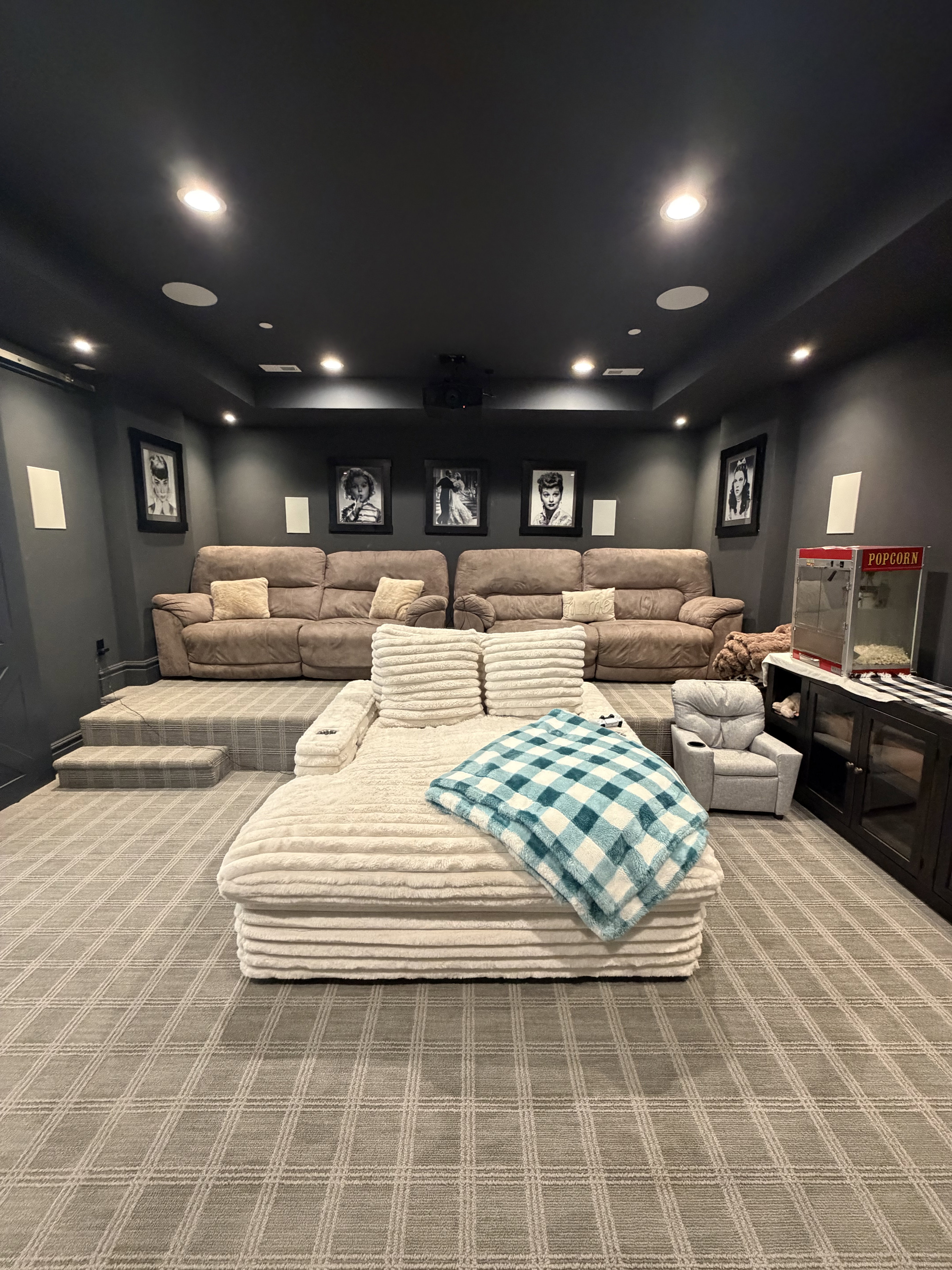 Dedicated entertainment room featuring layered seating, recessed ceiling lighting, wall-mounted speakers, a ceiling-mounted projector, and patterned carpet flooring