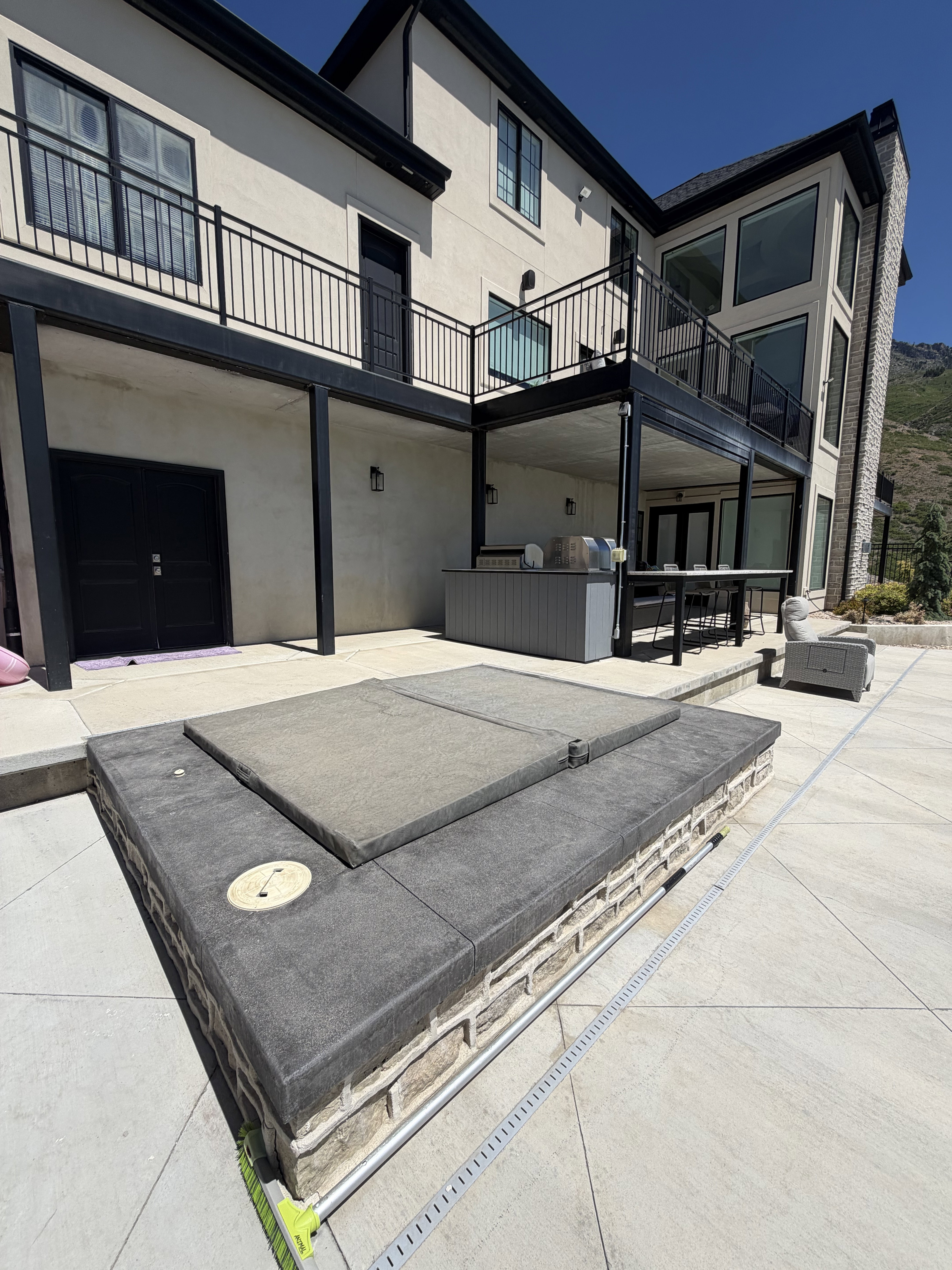 Expansive outdoor patio featuring a built-in hot tub, an outdoor kitchen with a grill, and substantial upper-level balconies with black railings