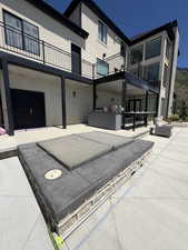 Expansive outdoor patio featuring a built-in hot tub, an outdoor kitchen with a grill, and substantial upper-level balconies with black railings