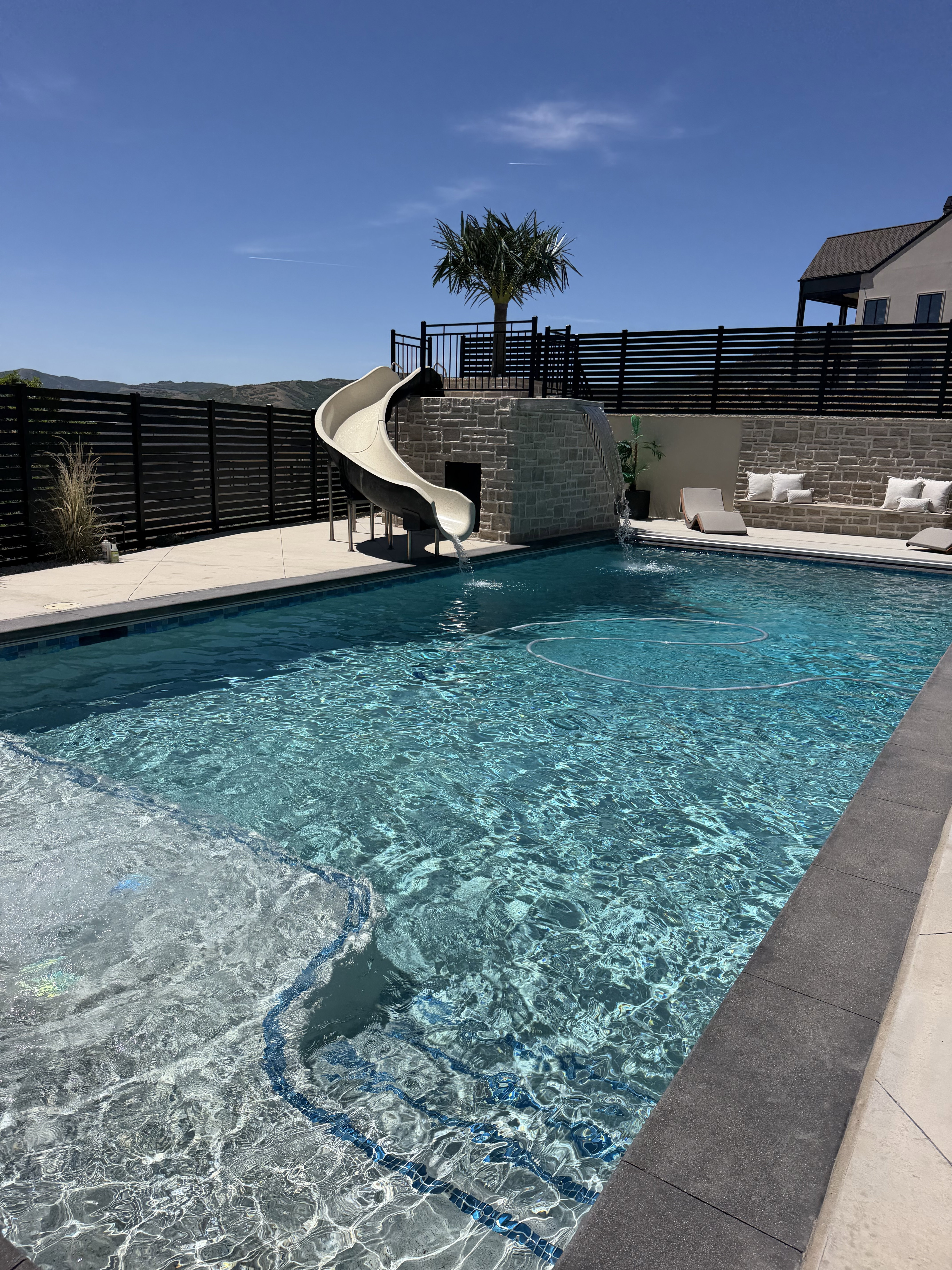 Rectangular swimming pool featuring integrated steps and a stone-clad water slide