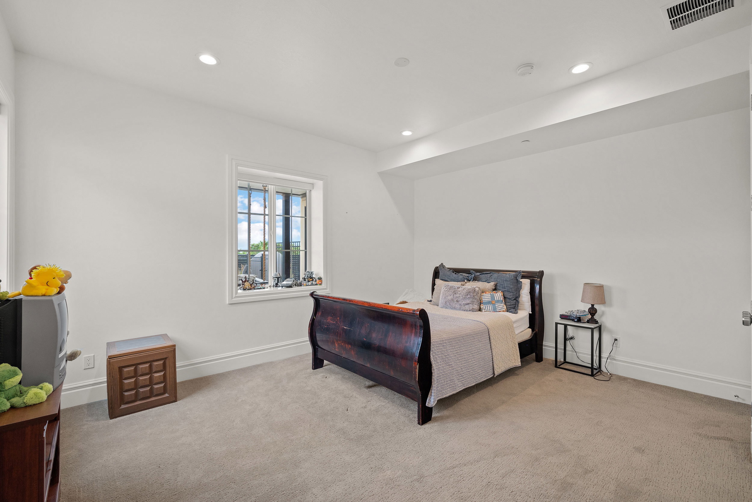 Spacious room featuring neutral carpeting, recessed lighting, and a window with white trim