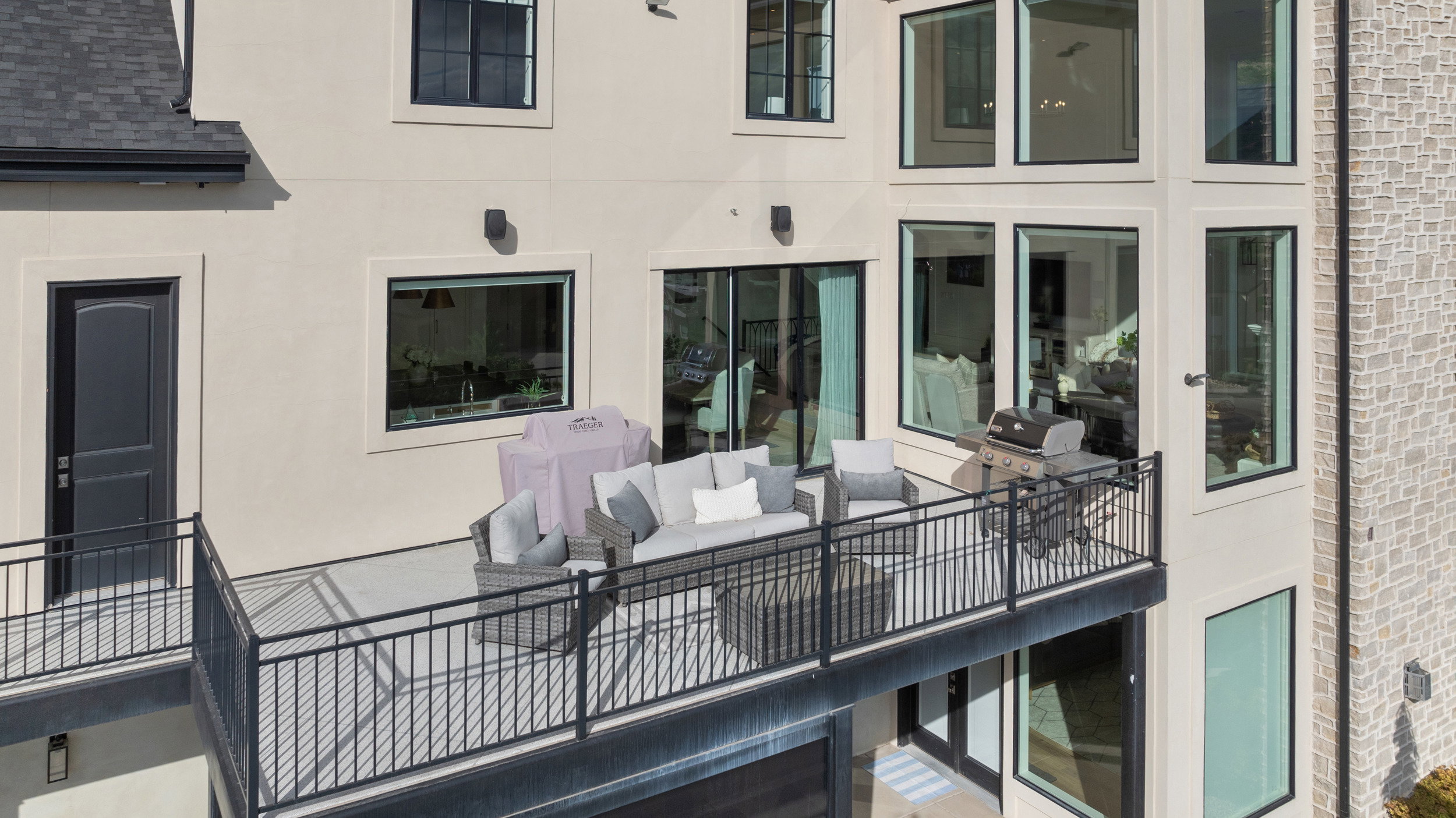 Upper-level balcony featuring black wrought iron railing, a light-colored stucco exterior, and multiple large windows with black trim