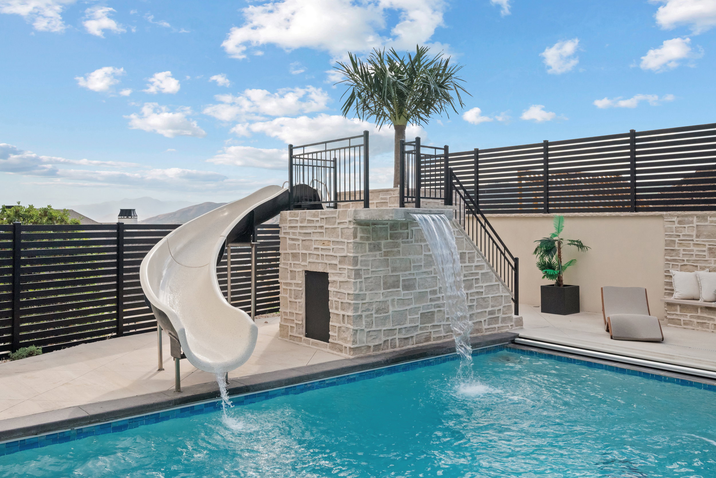 Swimming pool with a built-in slide and stone-clad waterfall feature