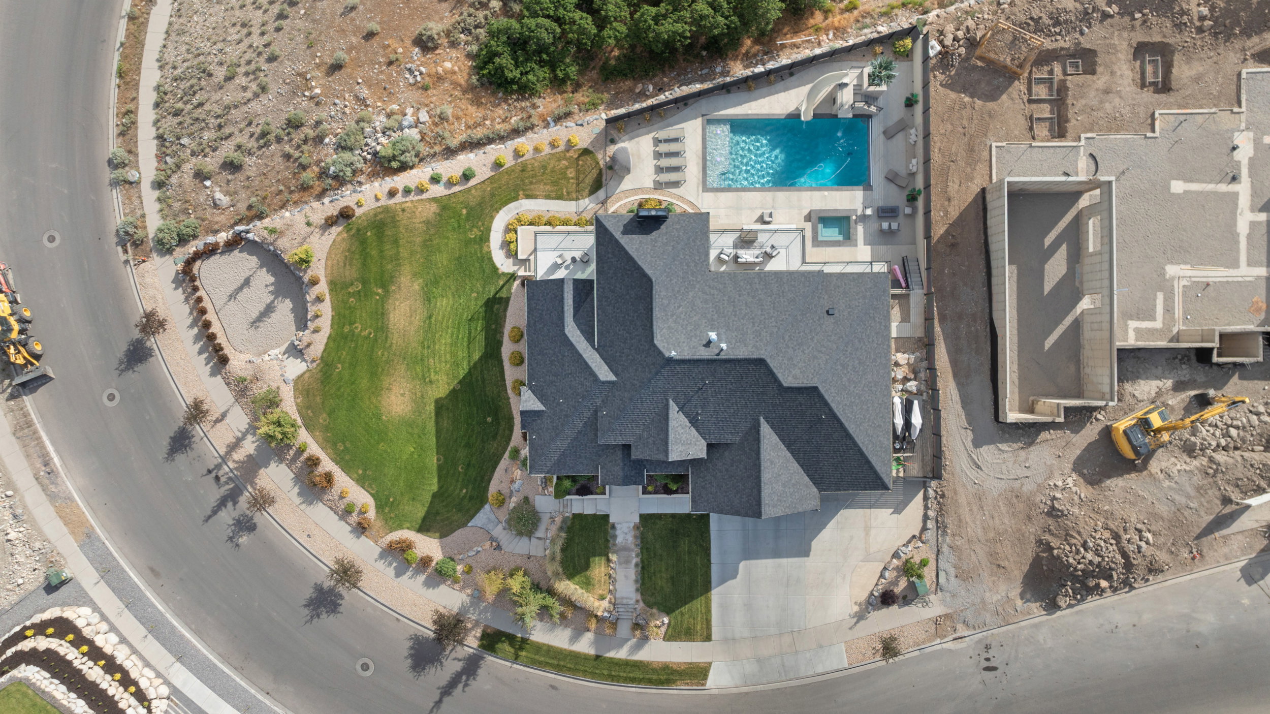 Expansive property featuring a multi-gabled dark shingle roof, a generously sized inground swimming pool with an attached hot tub, a manicured lawn, and a paved driveway