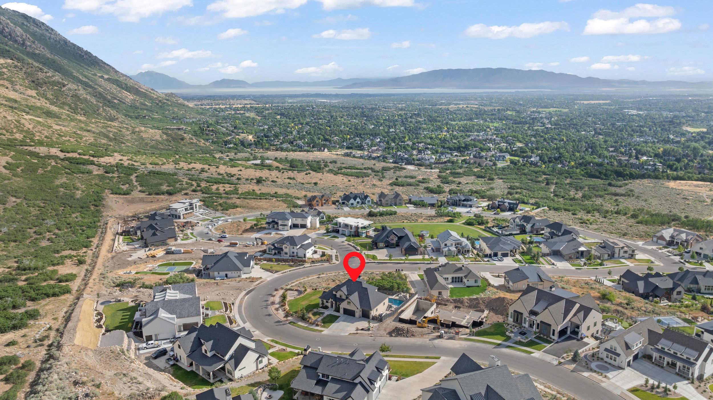 Aerial perspective of a hillside residential development featuring a mountain backdrop and distant body of water