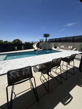Outdoor entertaining space featuring a built-in bar, pool with water feature and slide, stone retaining walls, and privacy fencing